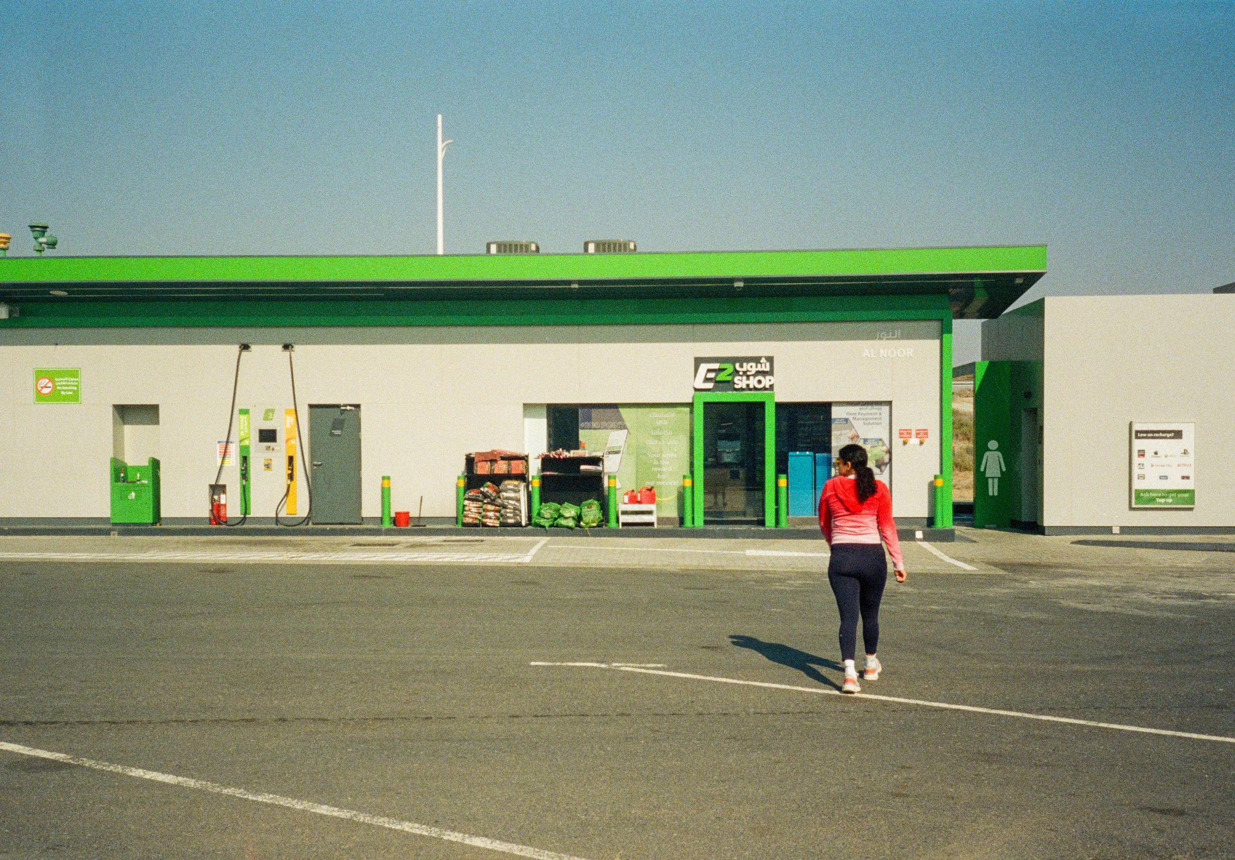 Woman crossing a petrol station forecourt in bright sunlight