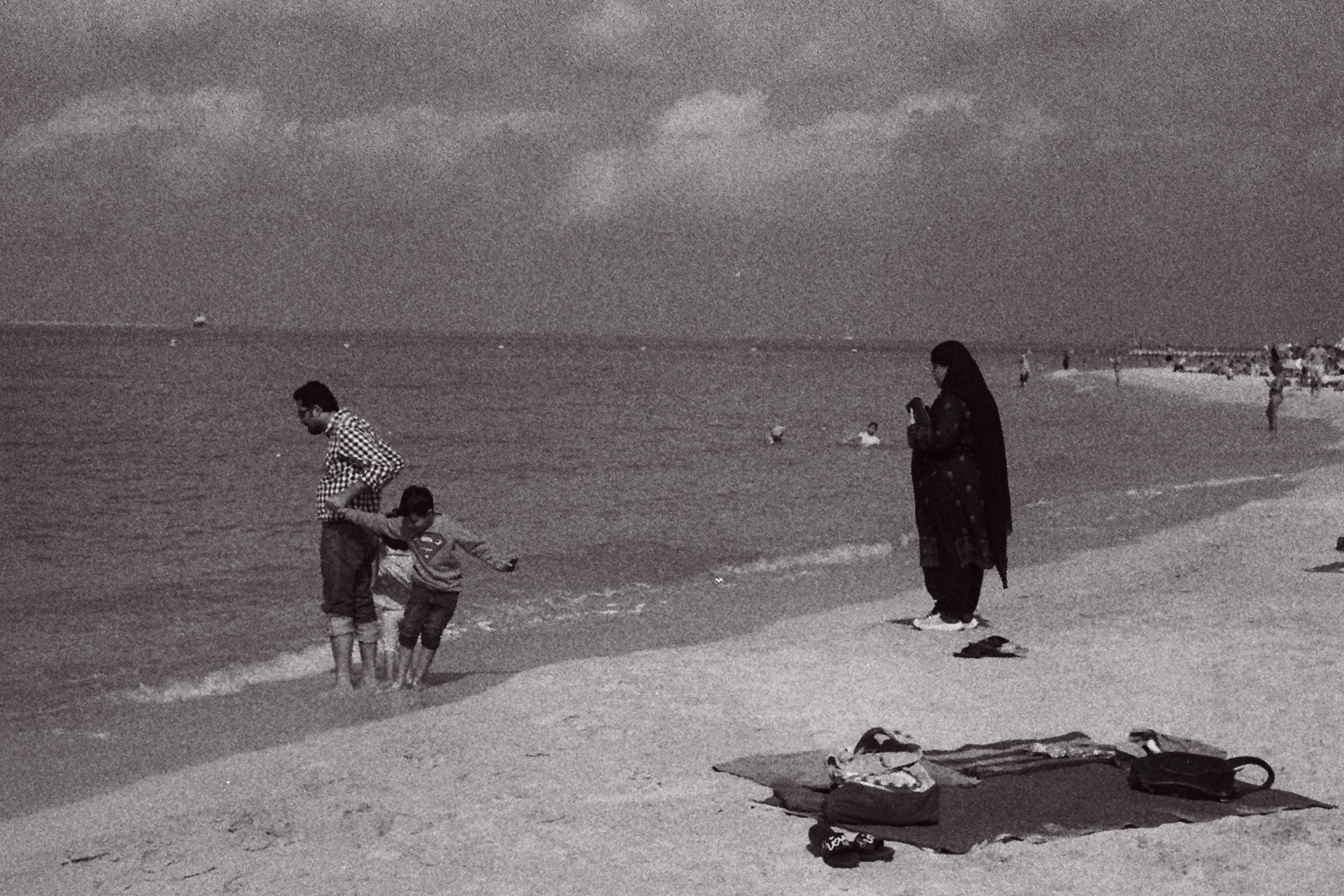 Father and boy at the waterline while a veiled woman photographs them