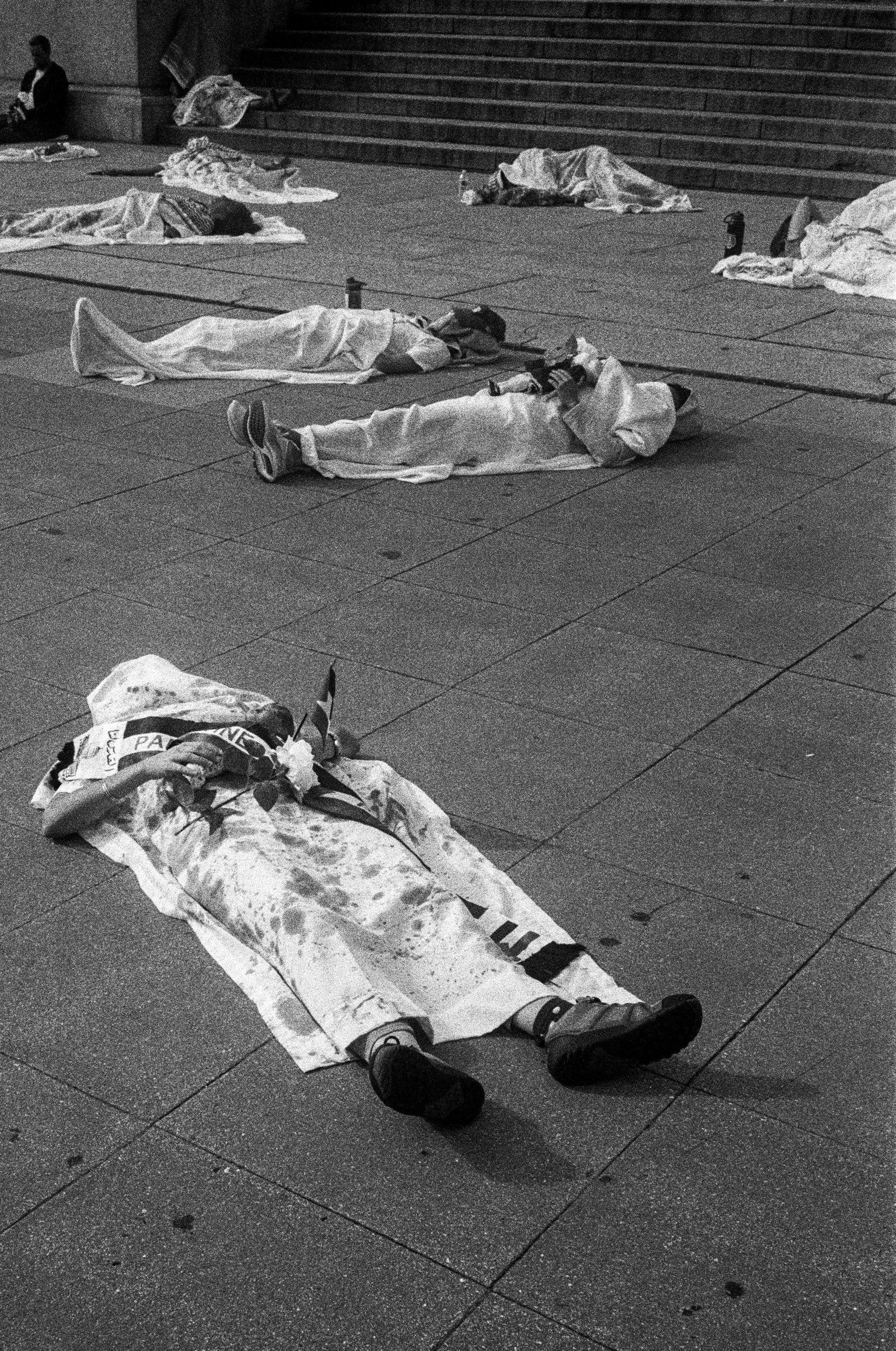 Die-in protest in Washington: shrouded bodies on the pavement, one with a carnation