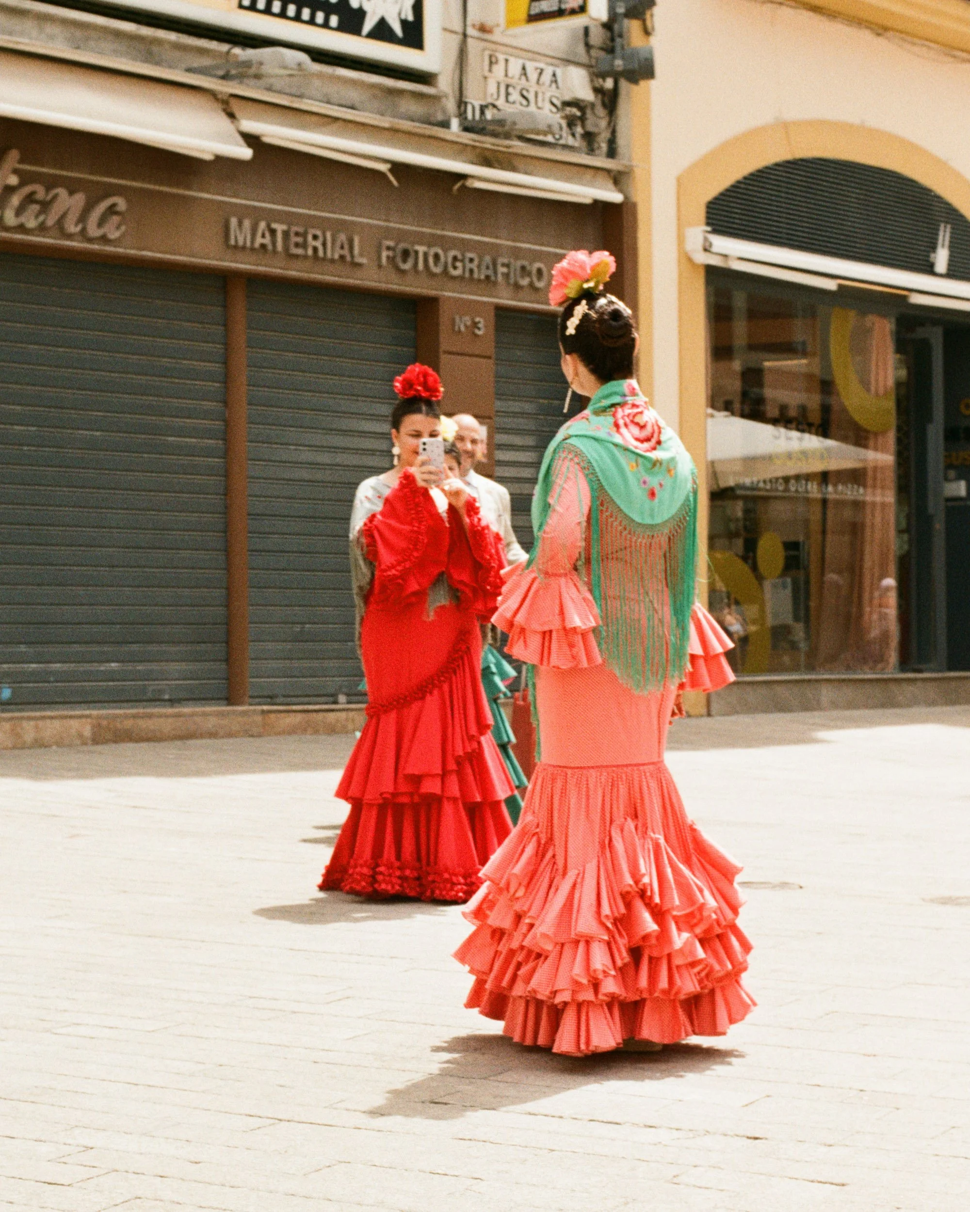 Two flamencas in red dresses photographing each other outside a camera shop, Seville