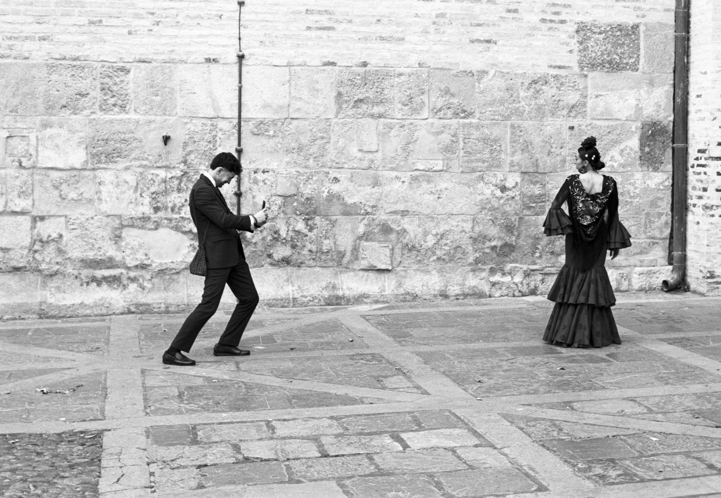 A photographer and a flamenca passing before a great stone wall, Seville