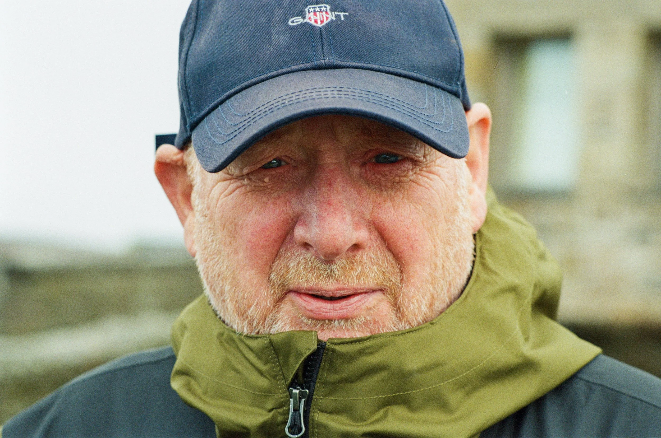 Portrait of a weathered face beneath a navy cap on the coast