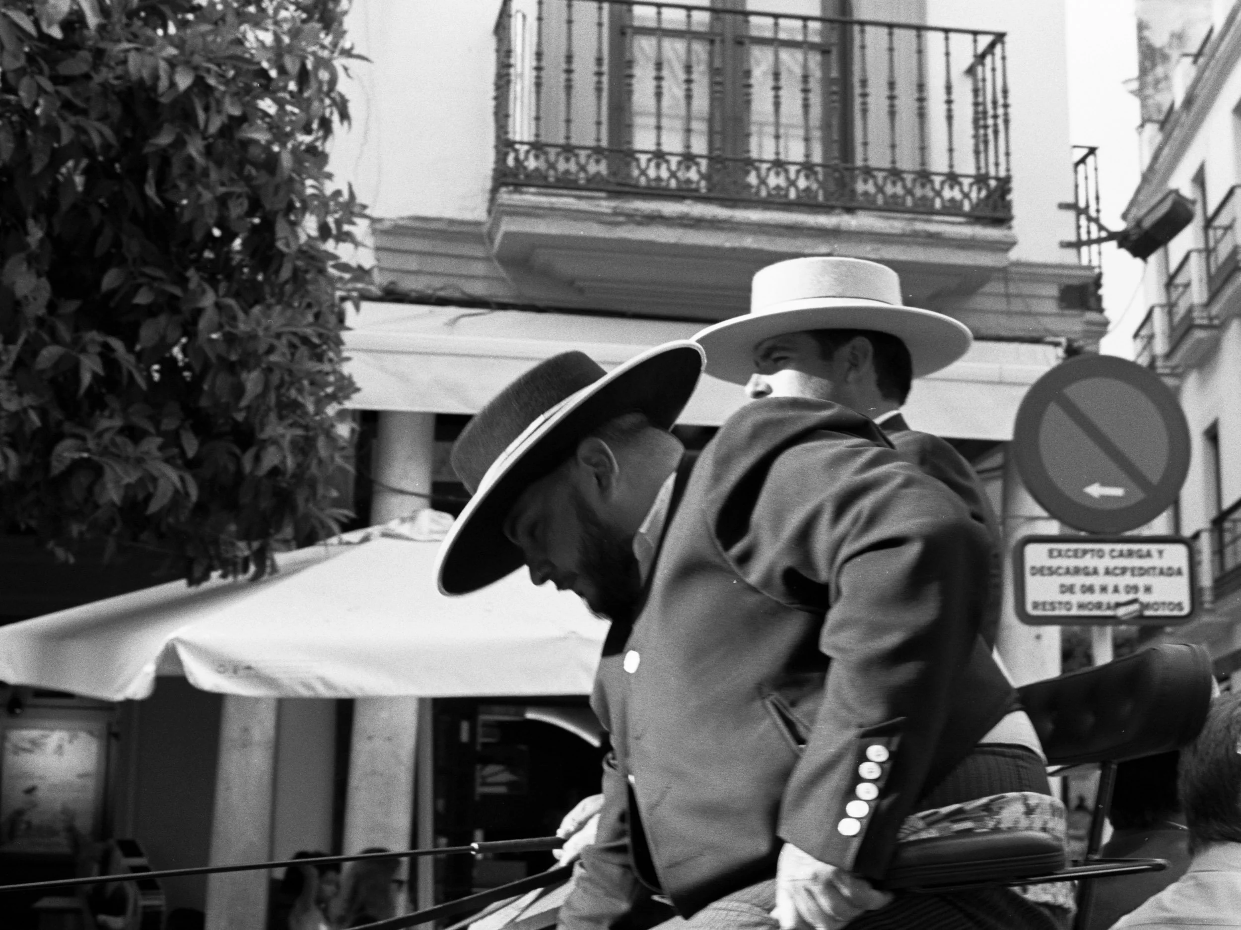 Two carriage men in wide-brimmed hats beneath a no-parking sign, Seville