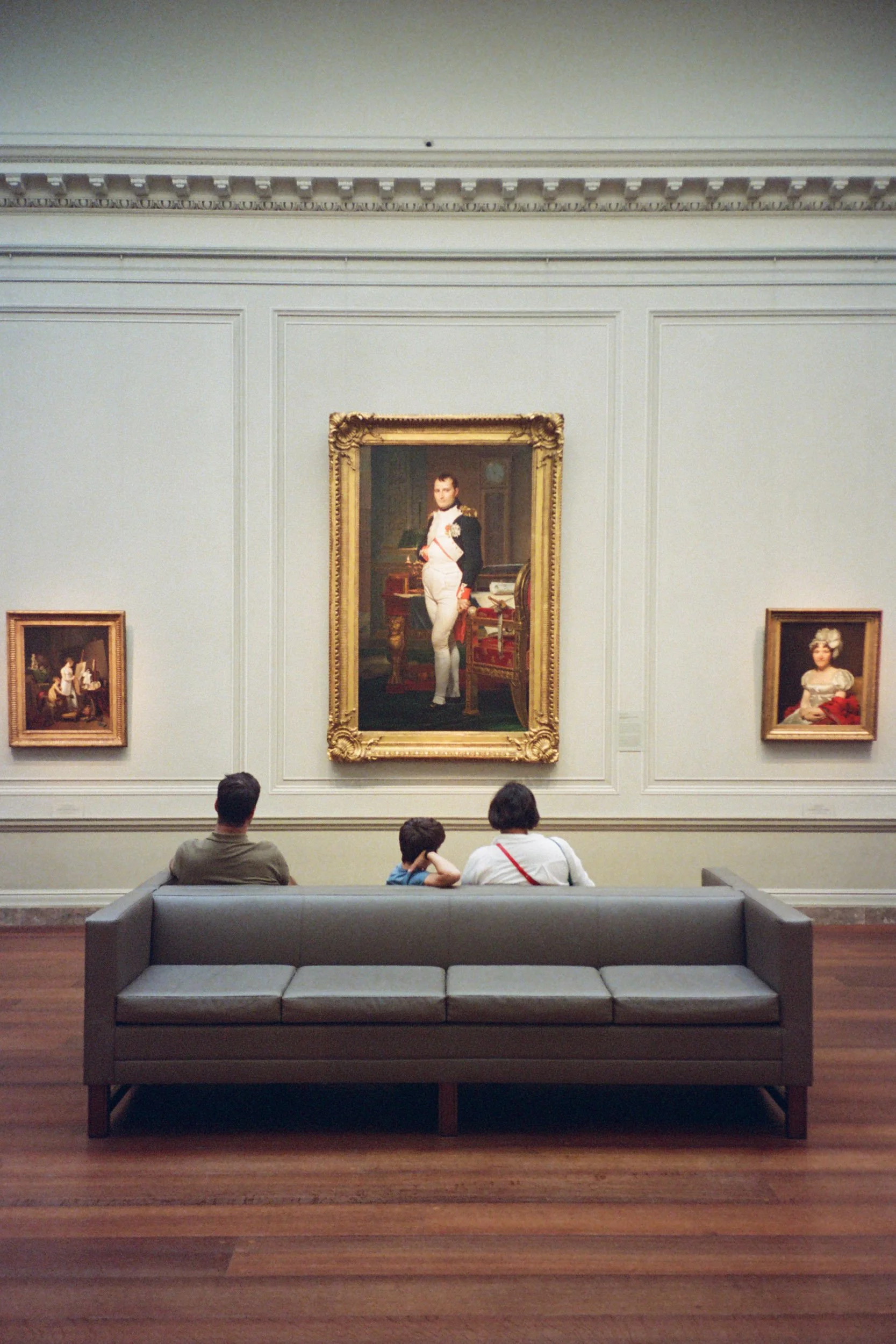 Family on a bench beneath the portrait of Napoleon in a museum gallery