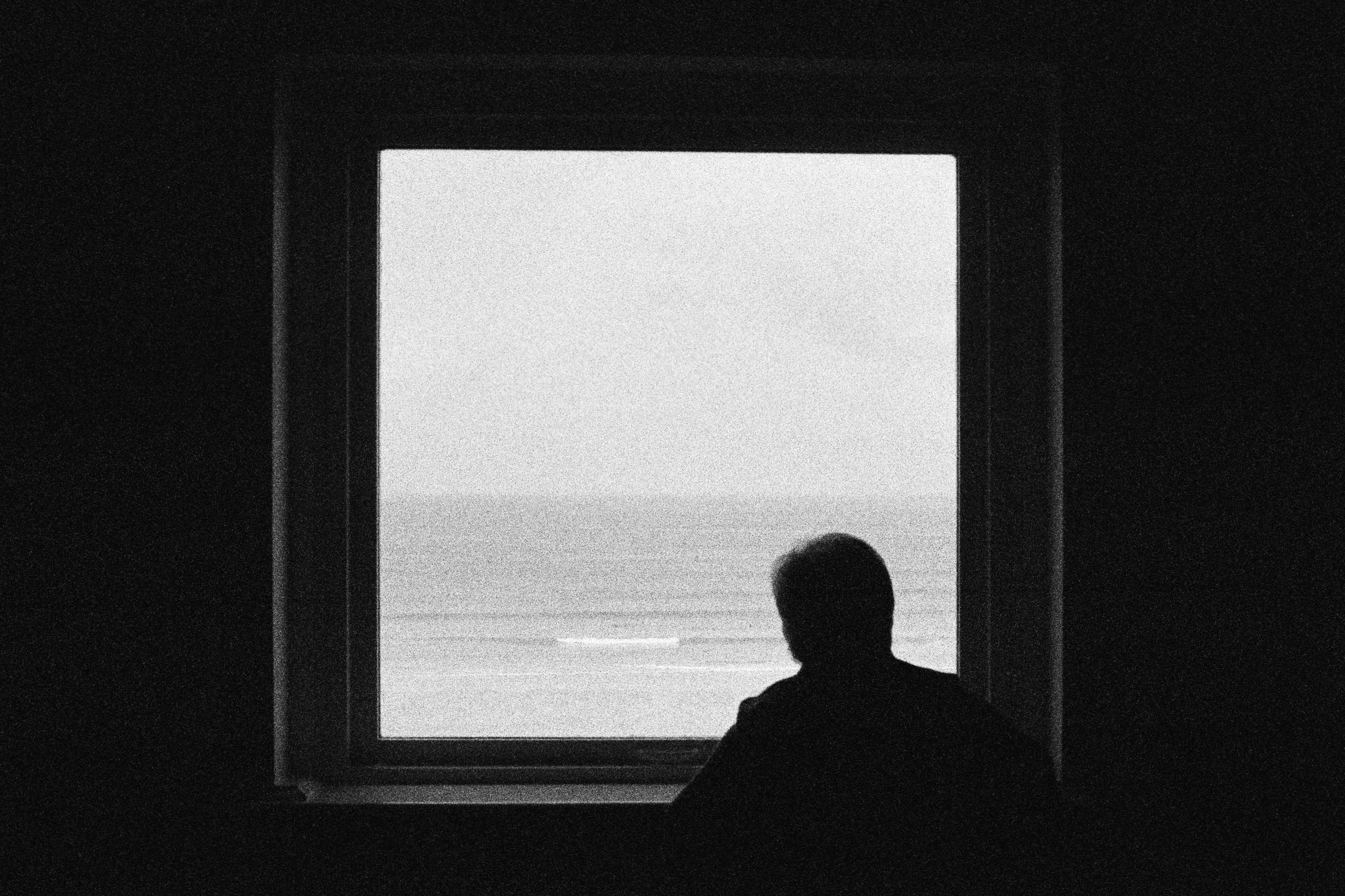 A silhouetted figure looks out at the sea through a bright window