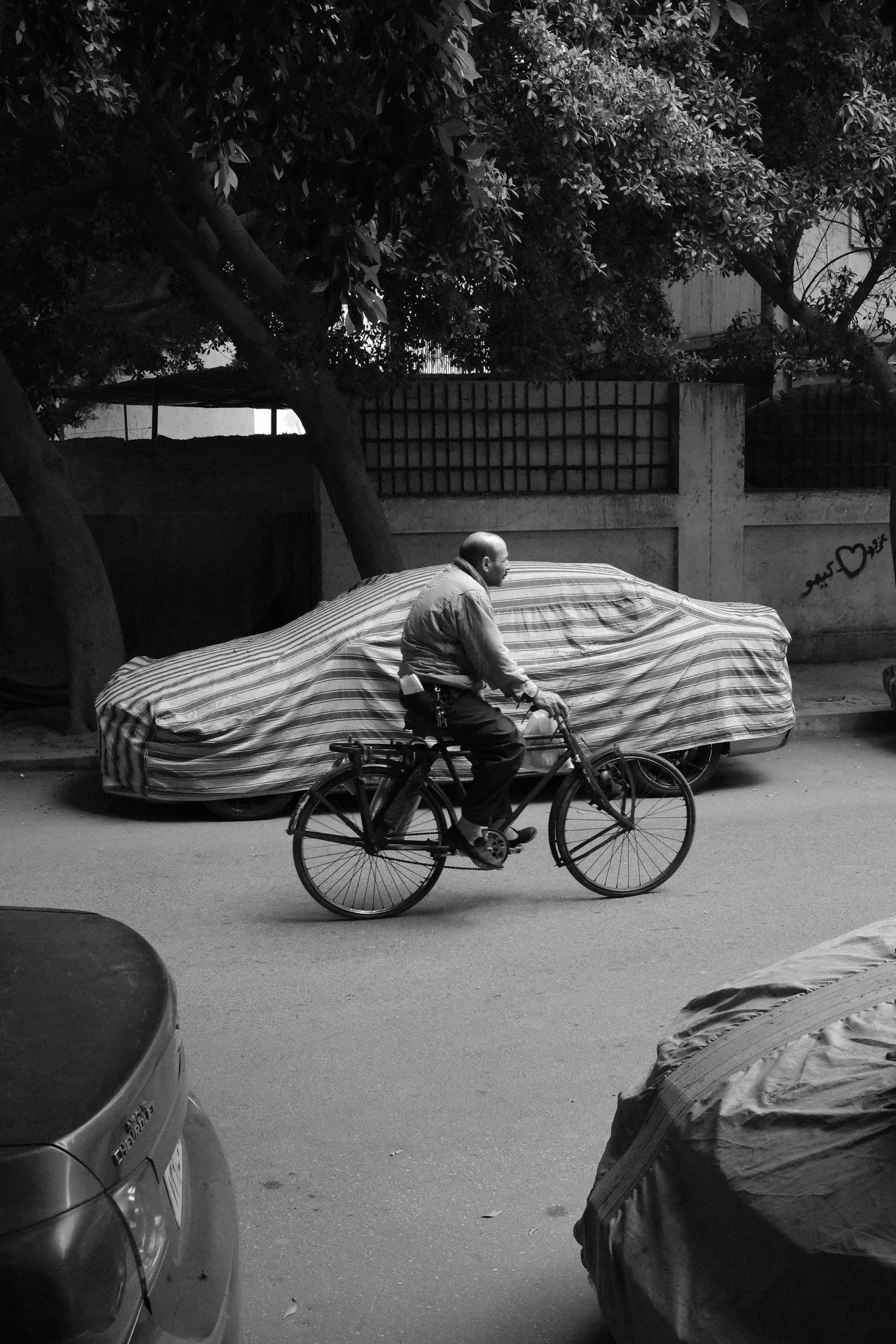 A cyclist passes a car sleeping under a striped cover, Cairo