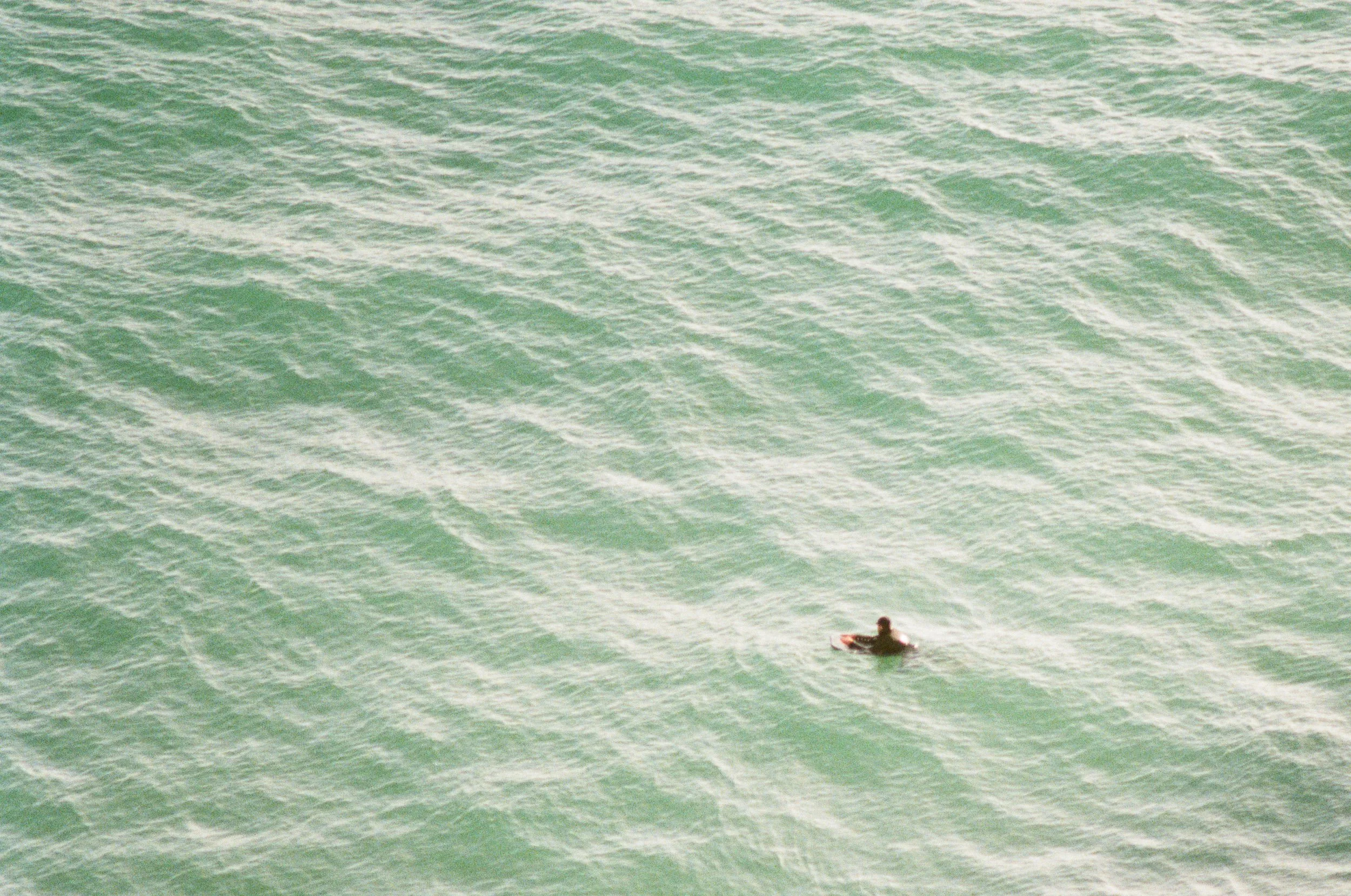 A lone surfer waiting in a vast green sea