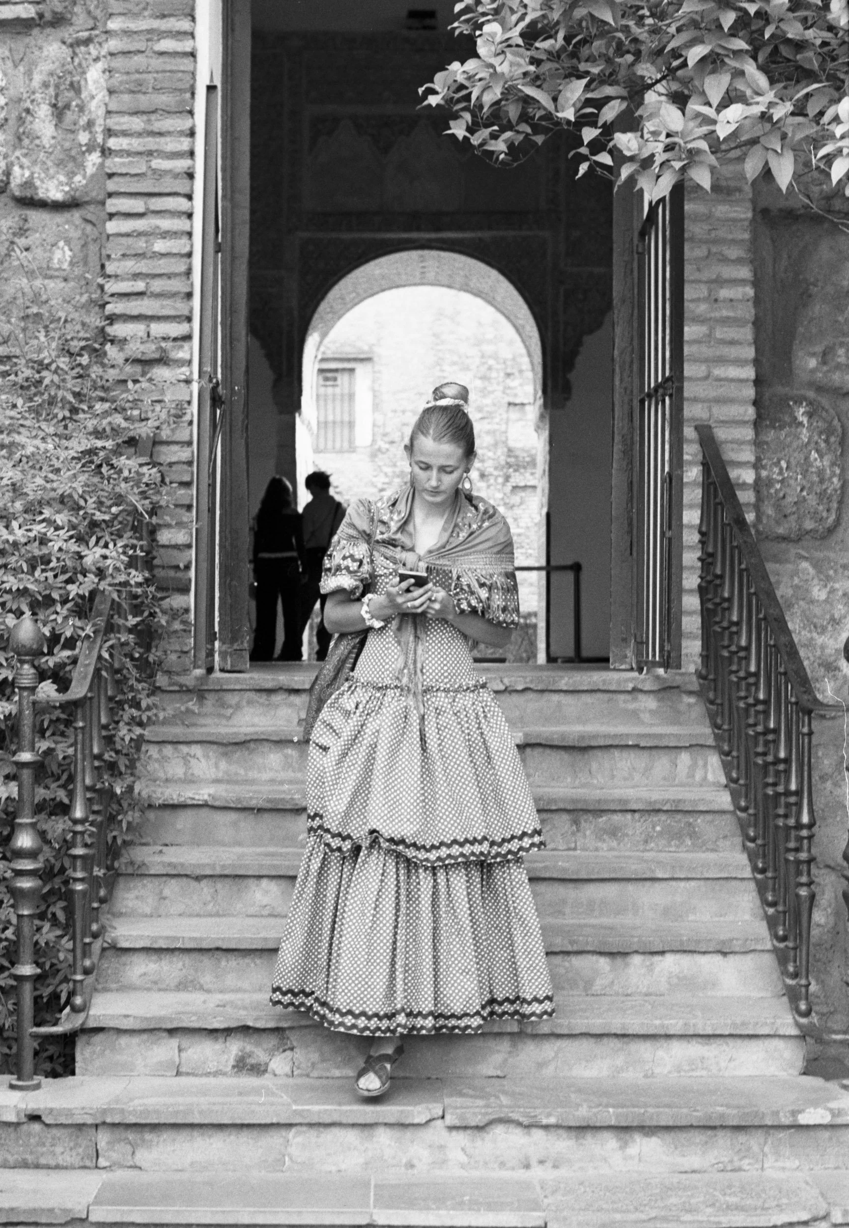 Flamenca in a polka-dot dress checking her phone beneath a Moorish arch, Seville