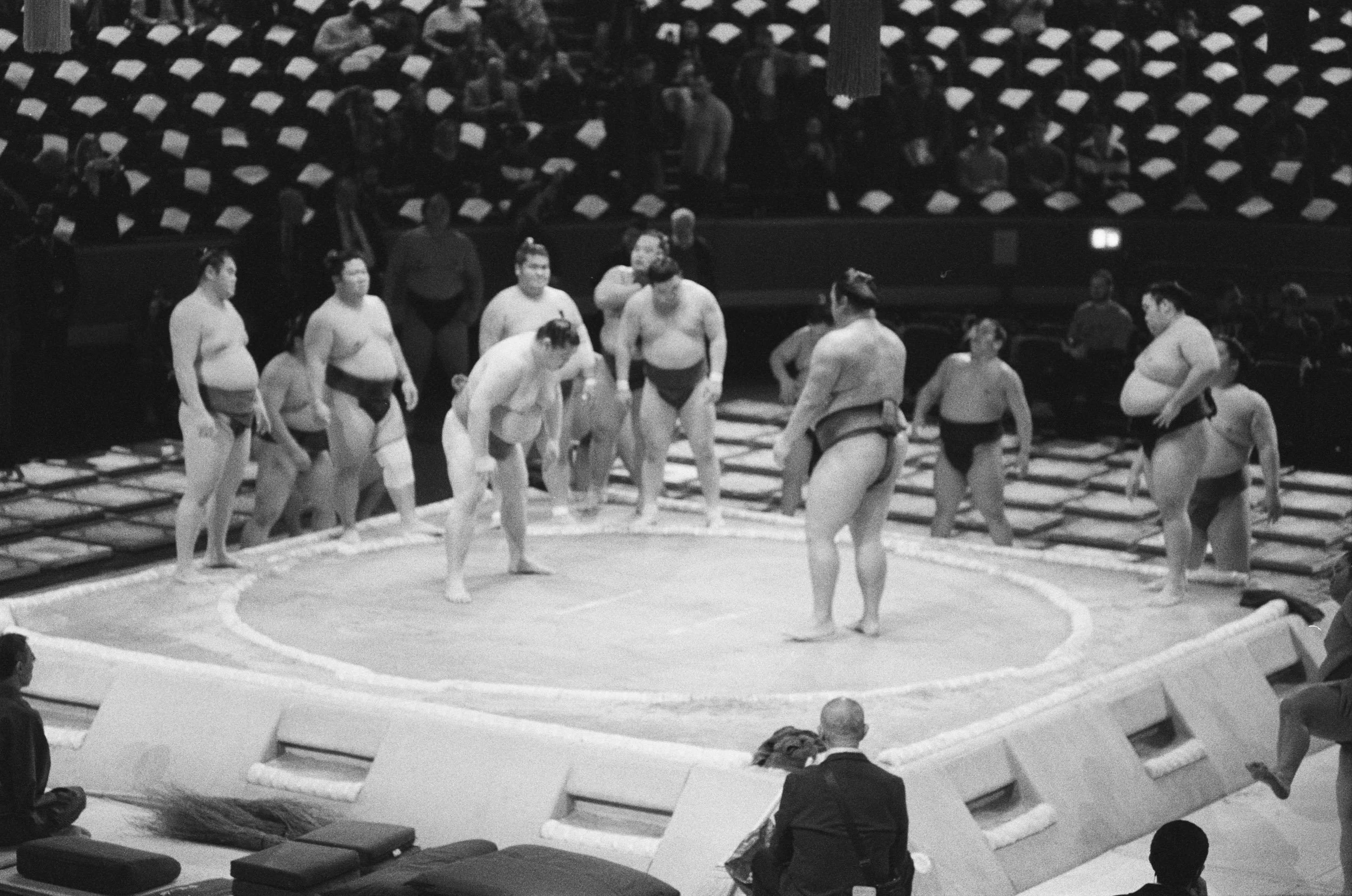 Wrestlers warming up on the dohyo in a half-empty hall