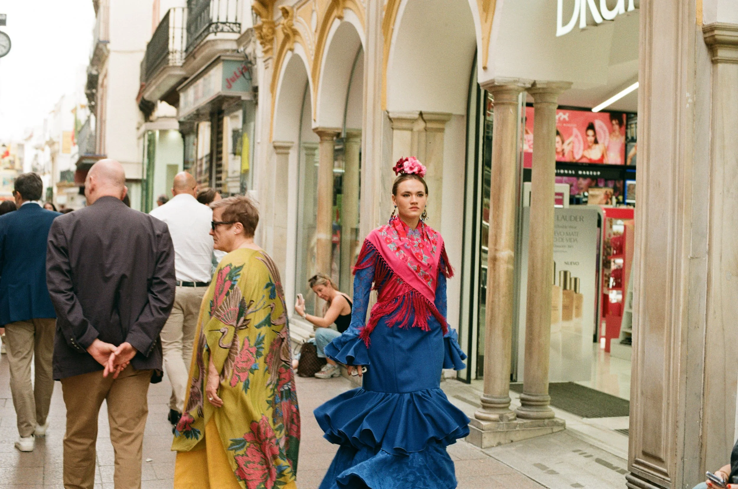Flamenca in a blue dress striding through a shopping colonnade, Seville