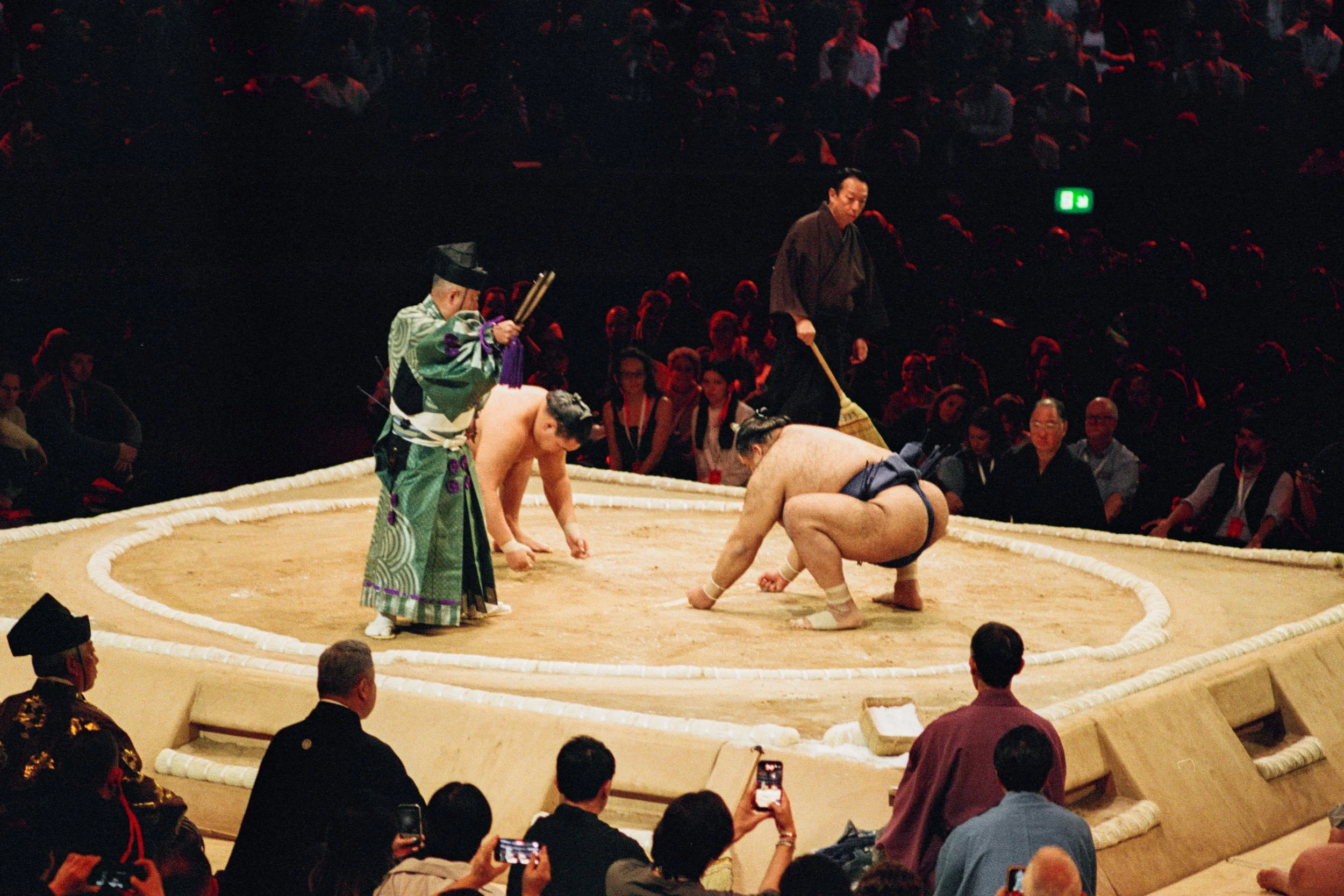 Sumo wrestlers face off while the crowd raise their phones