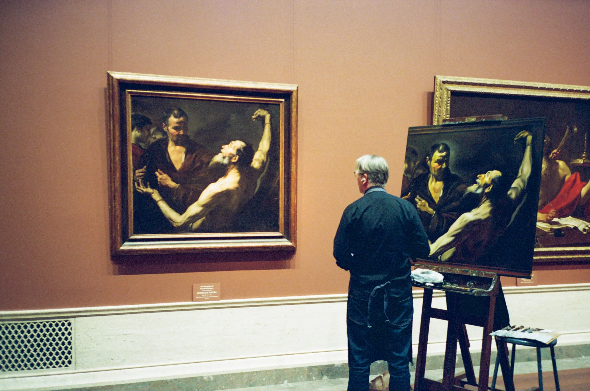 A copyist at his easel beside the original painting in a museum