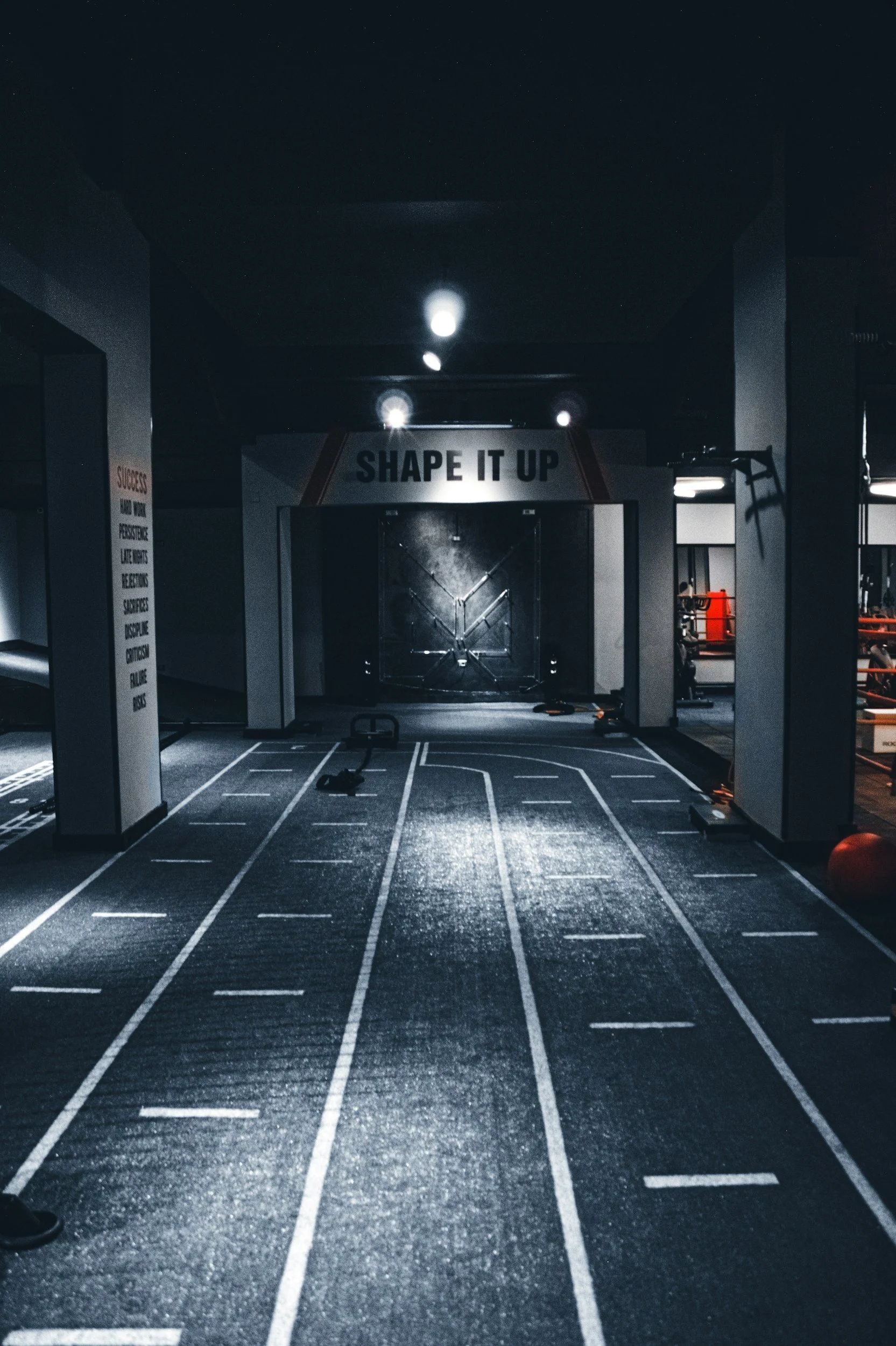 Empty gym with a designated workout lane, exercise equipment, and a sign that reads "Shape It Up."