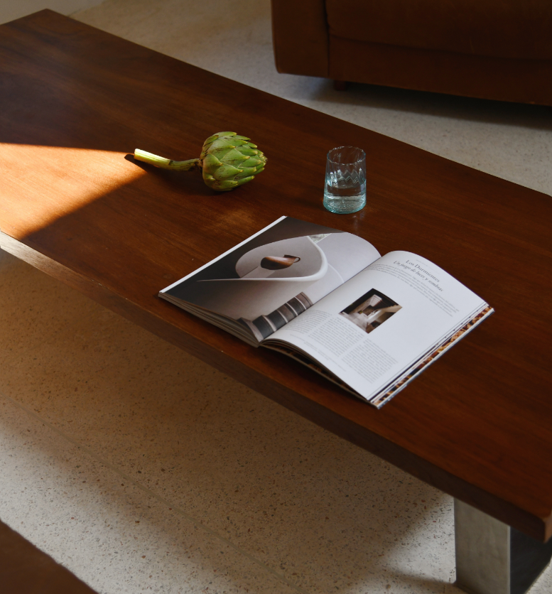 Une table en bois avec un artichaut, un verre d'eau et un magazine ouvert.