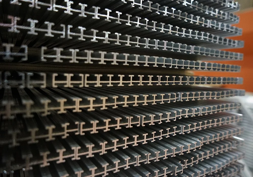 Close-up of stacked metal beams with cross-shaped ends in an industrial or manufacturing setting.