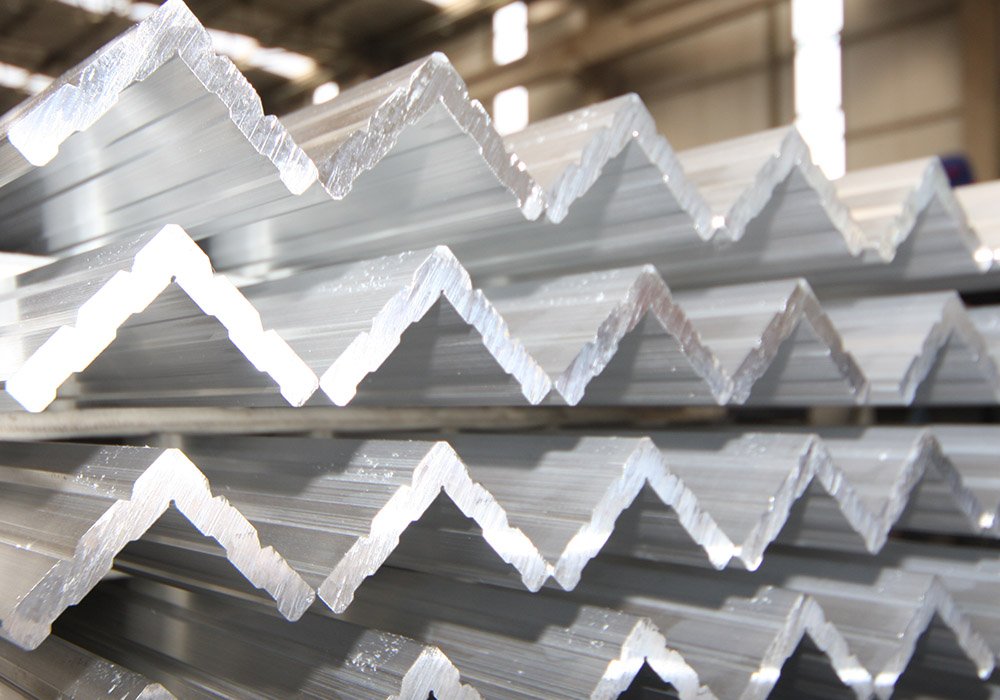Stack of aluminum or metal Z-shaped angle bars in a warehouse or factory setting.