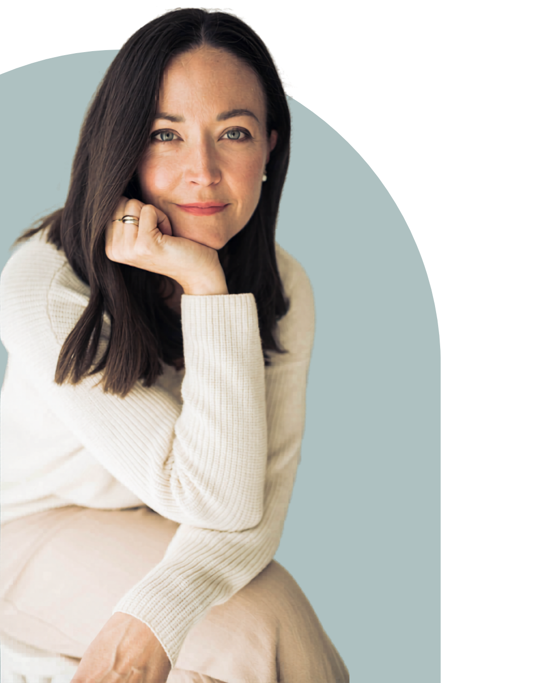 Portrait of a woman with long dark hair resting her chin on her hand, wearing a cream-colored sweater, looking at the camera with a slight smile.