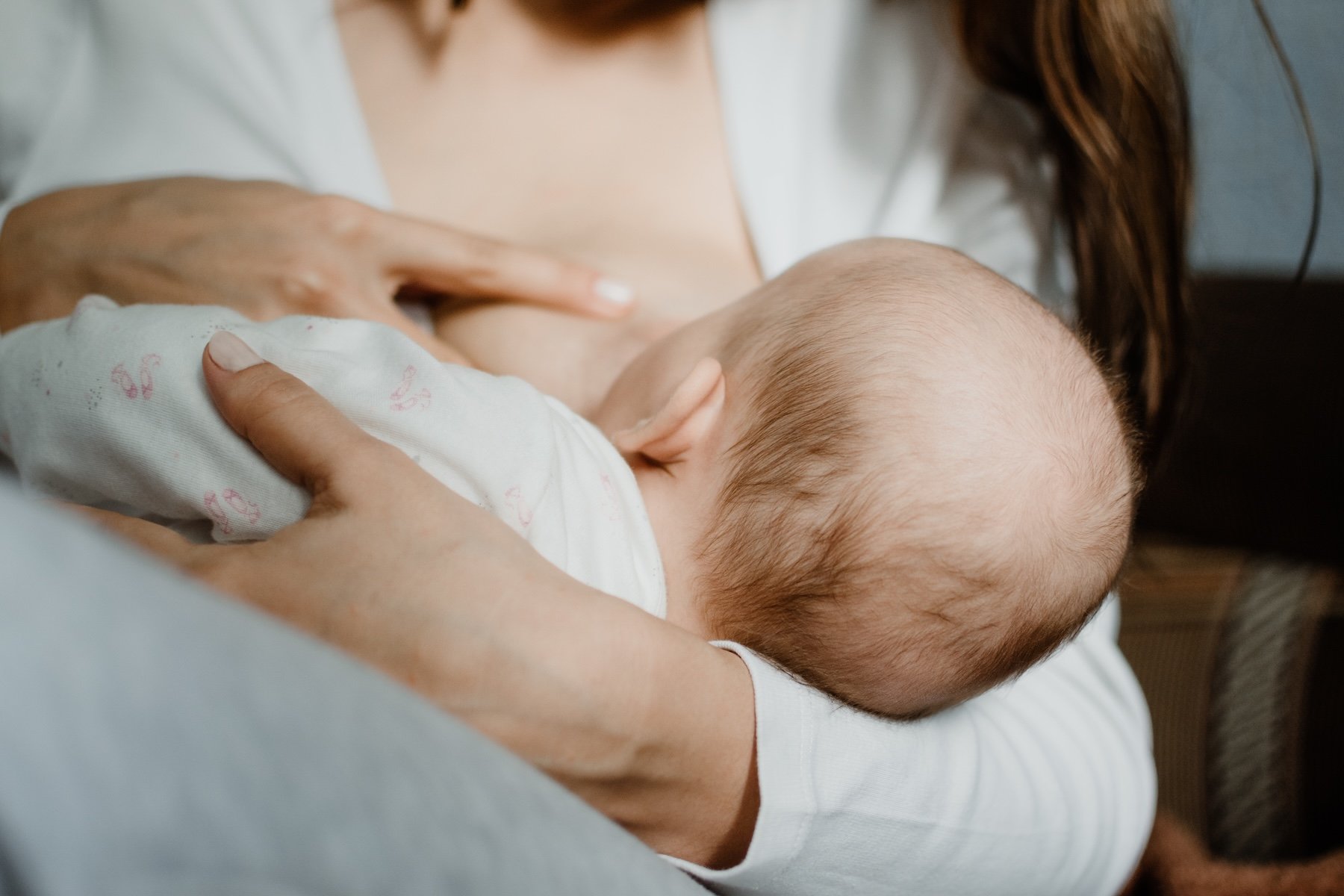 Close-up of a person breastfeeding a baby, focusing on the baby's head and the person's hands holding the baby while nursing.