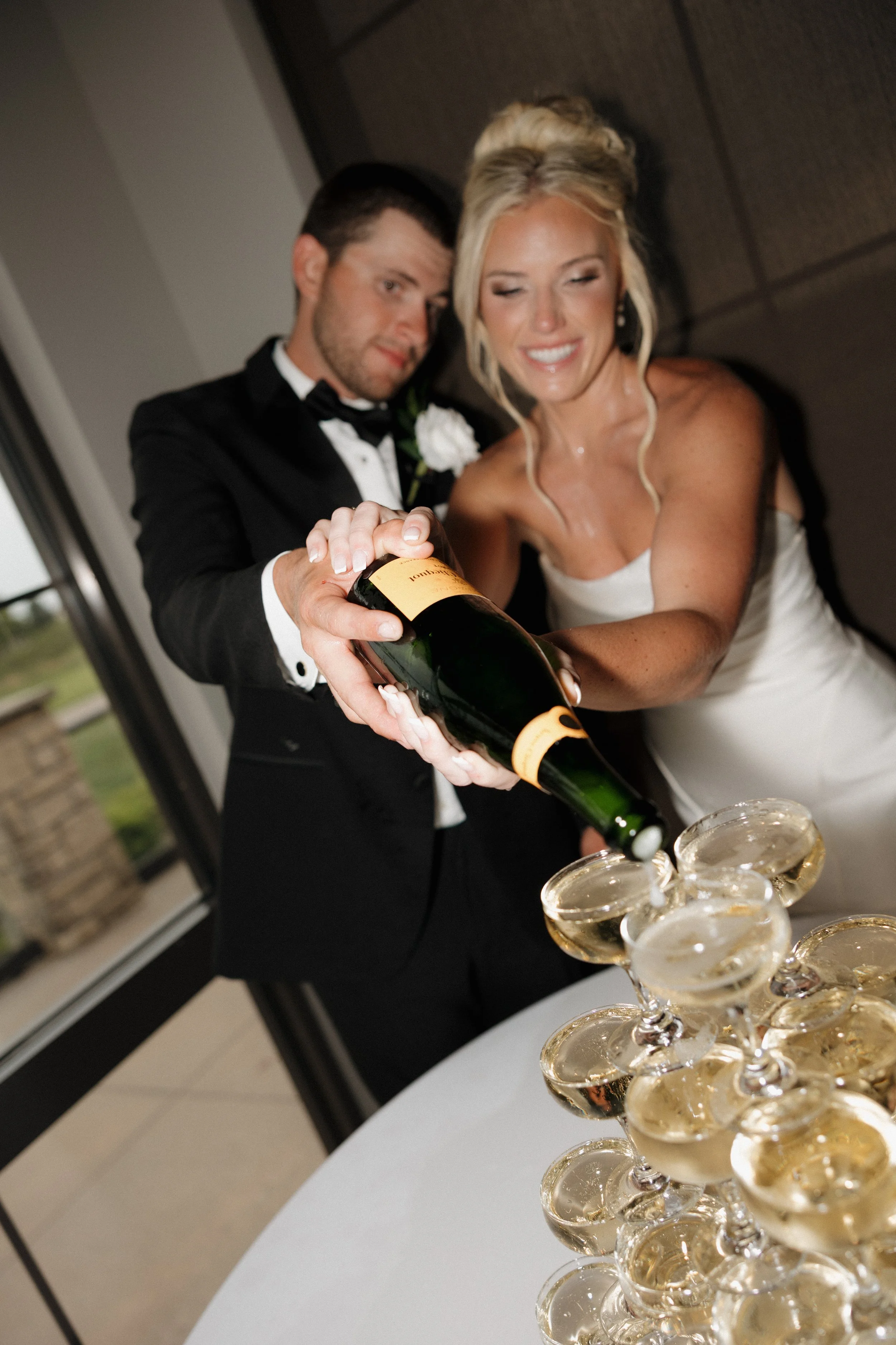 A bride and groom pouring champagne into a tower of glasses during a wedding celebration.