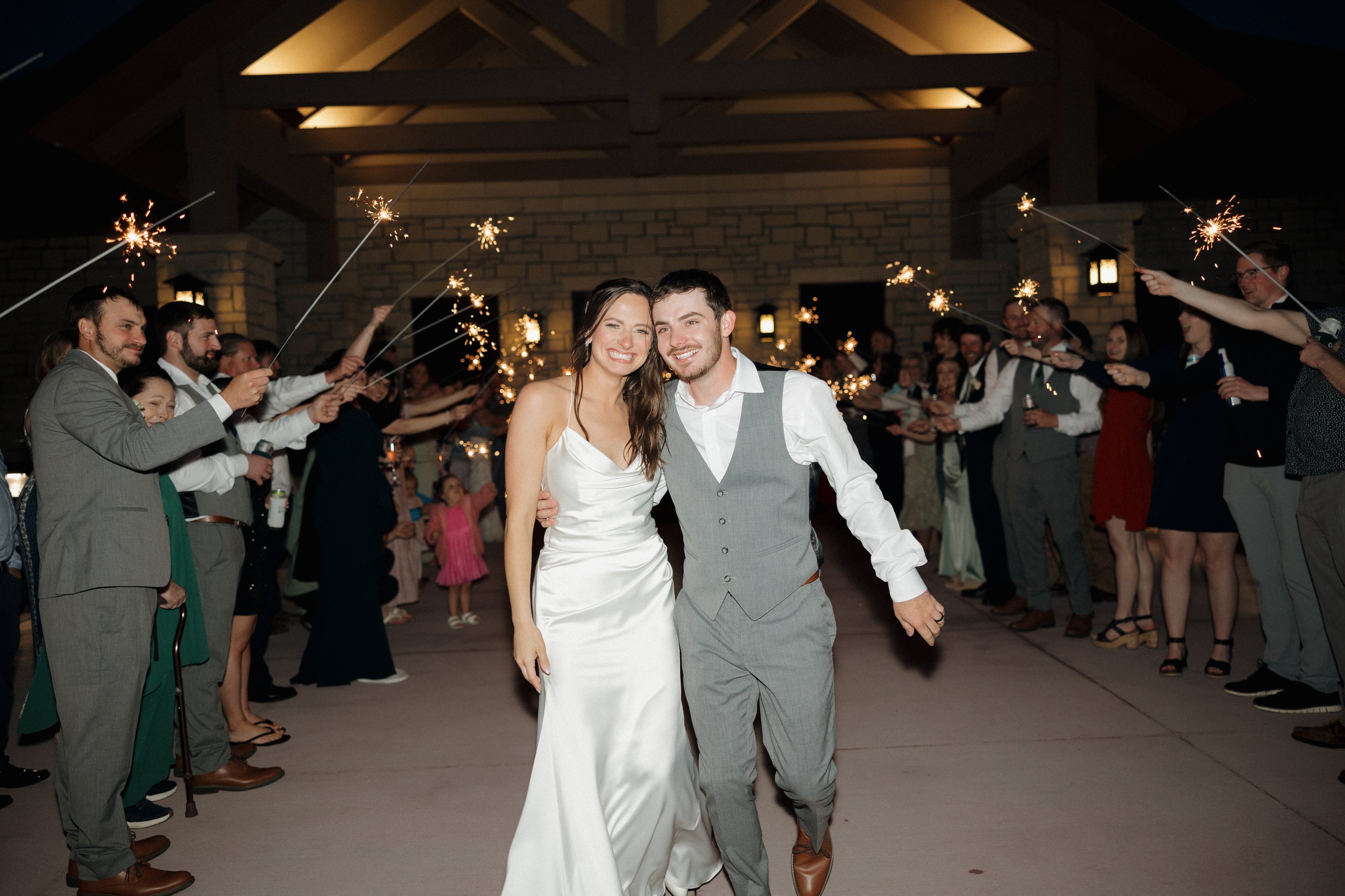 A bride and groom dancing at their wedding reception while guests hold sparklers in the background.