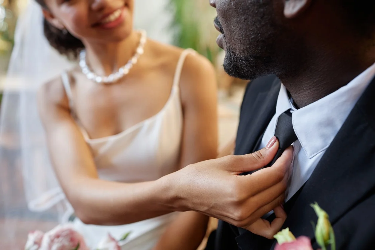 Woman in wedding dress adjusting the man's collar in a wedding setting.