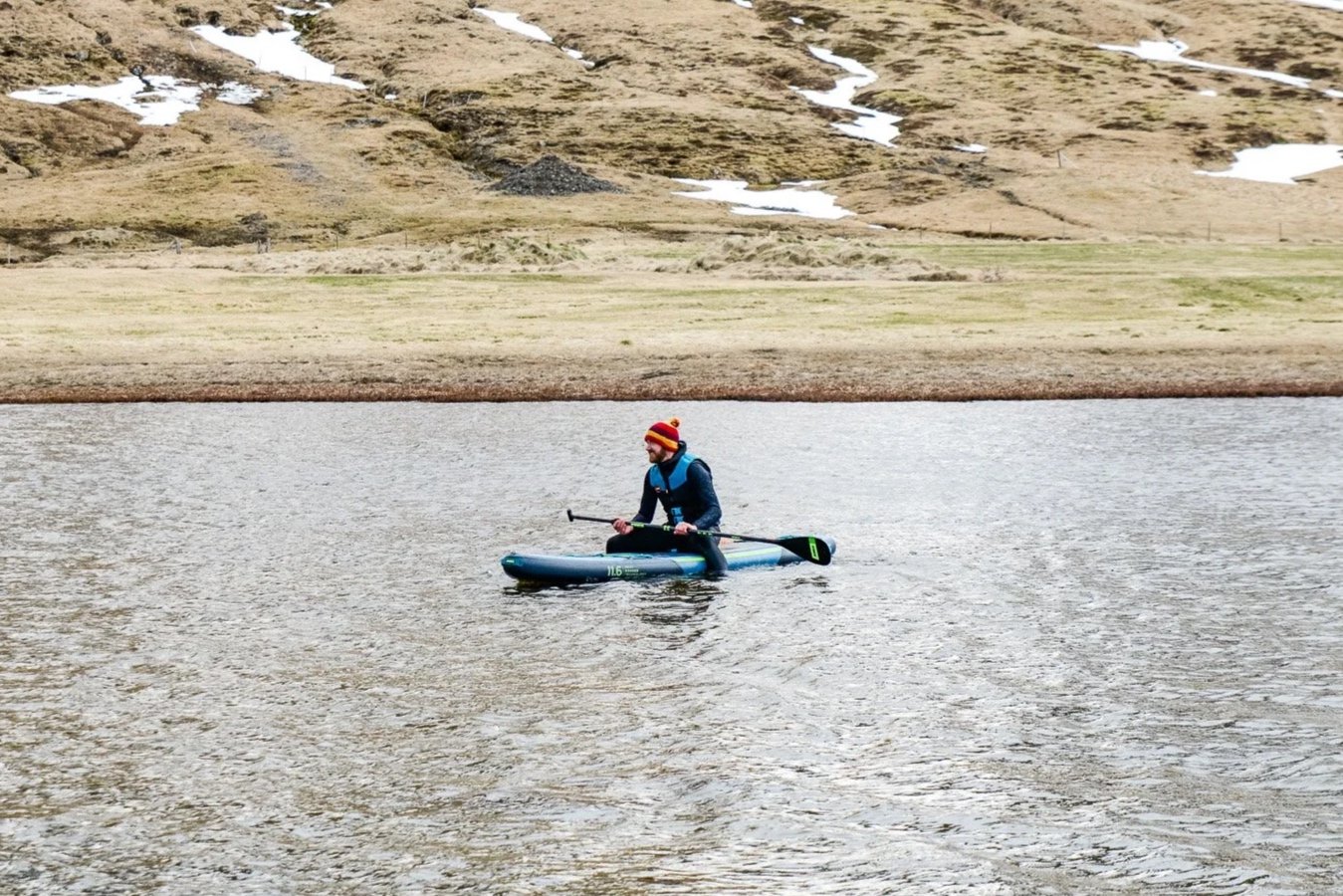 Man paddleboarding on a lake with mountainous terrain in the background.