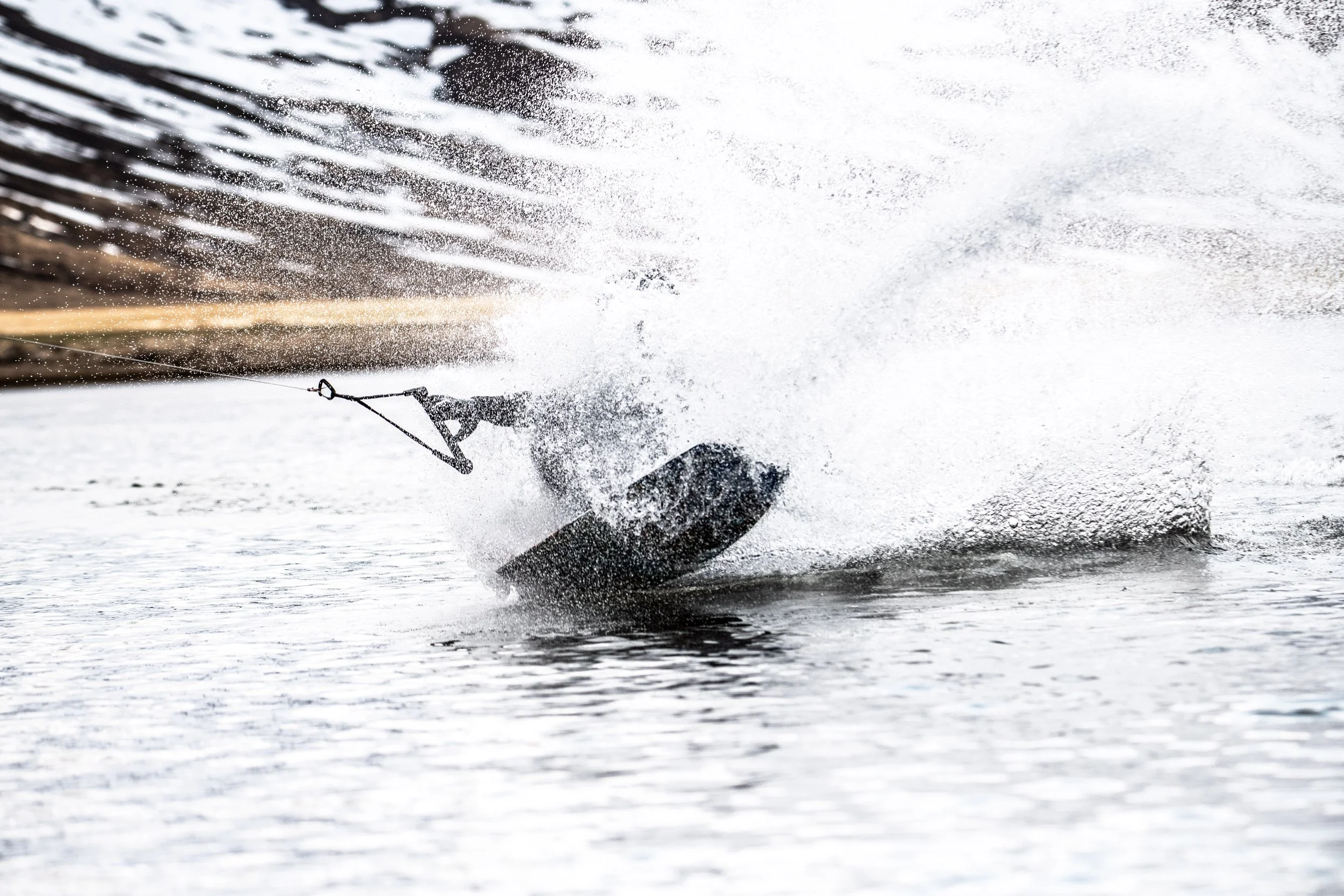A skier on snow-covered ground makes a sharp turn, creating a spray of snow and water.