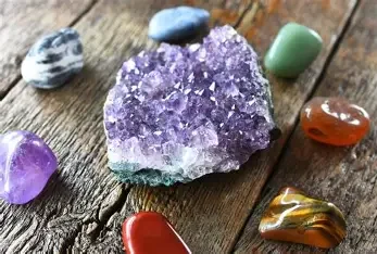 Various polished and raw gemstones, including a large purple amethyst cluster, placed on a wooden surface.