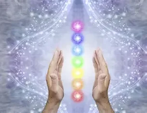 Two hands positioned around a vertical row of colorful, glowing orbs representing chakras, with a mystical, cosmic background.