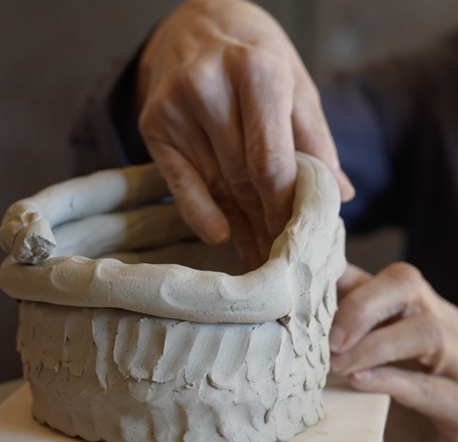 Close-up of an artist shaping clay to create a ceramic sculpture, focusing on their hands and the clay pot.