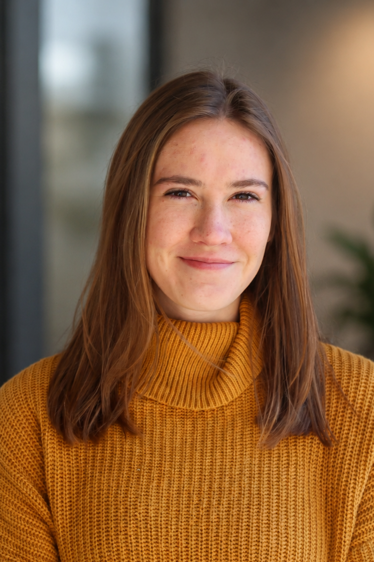 Close-up of a young woman with long brown hair wearing a mustard yellow turtleneck sweater, smiling softly.