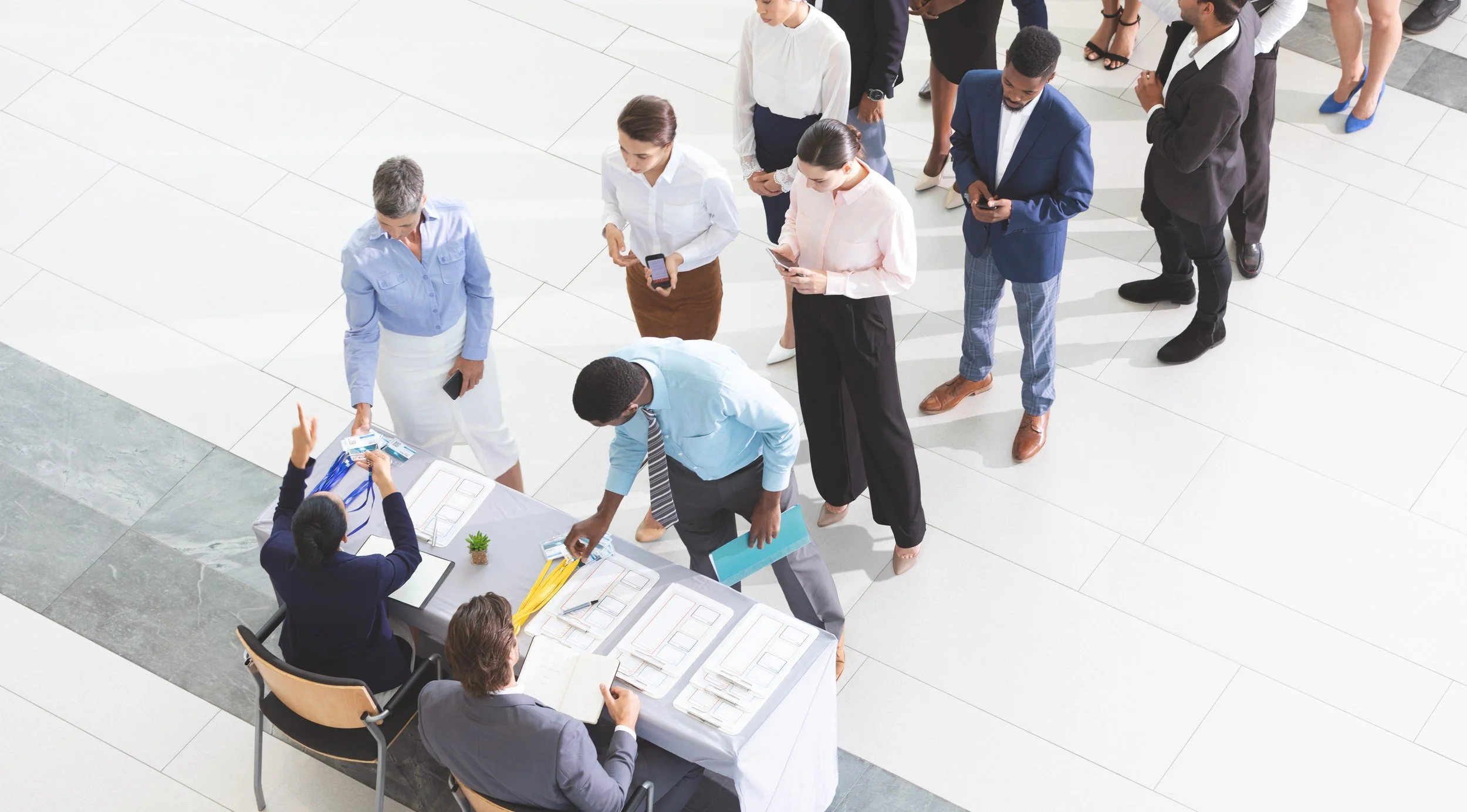 Business professionals standing in line at a registration or check-in desk in a modern office or conference setting.