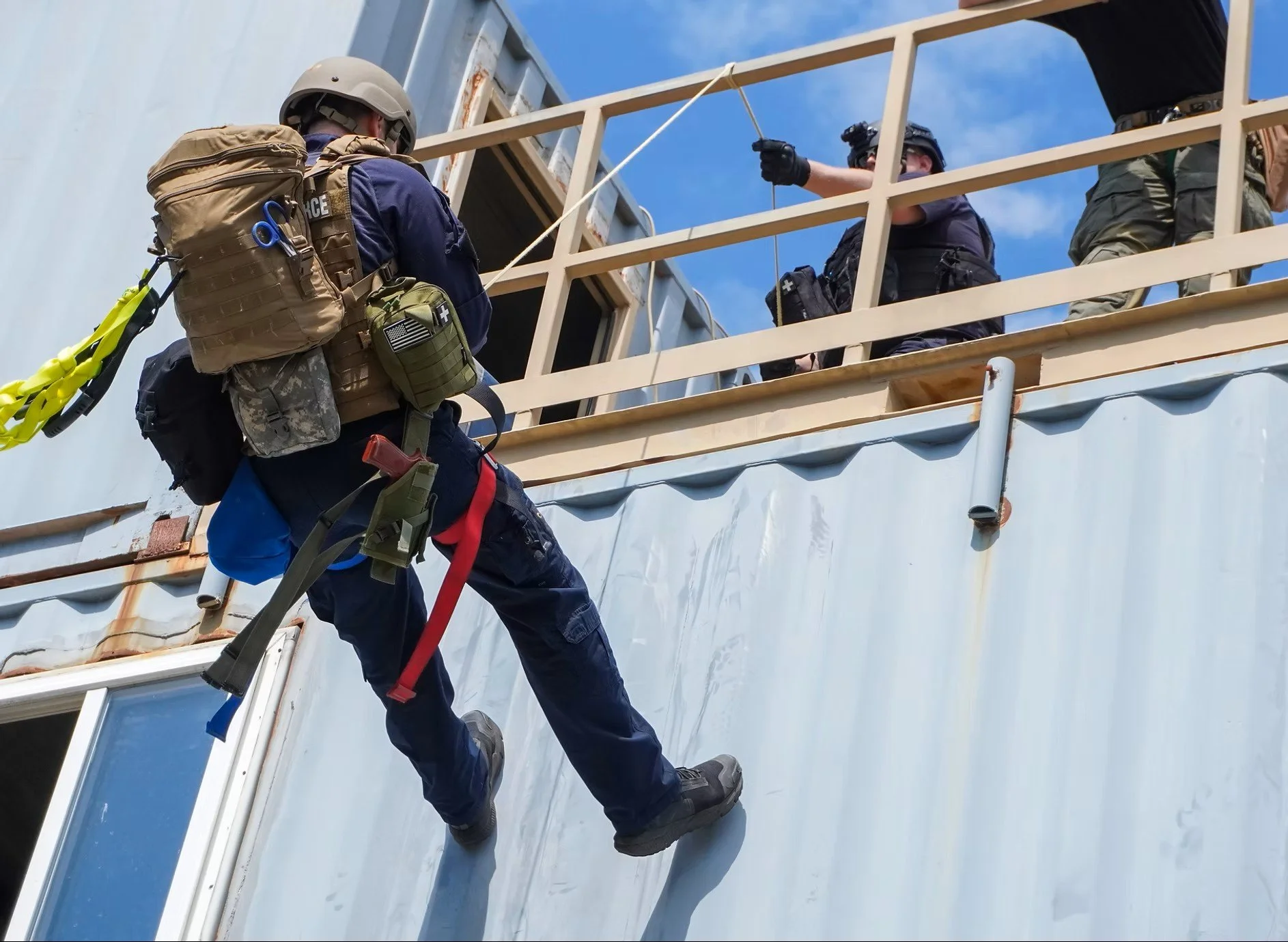 A tactical team member rappelling down a building during a training exercise, wearing tactical gear and a helmet.