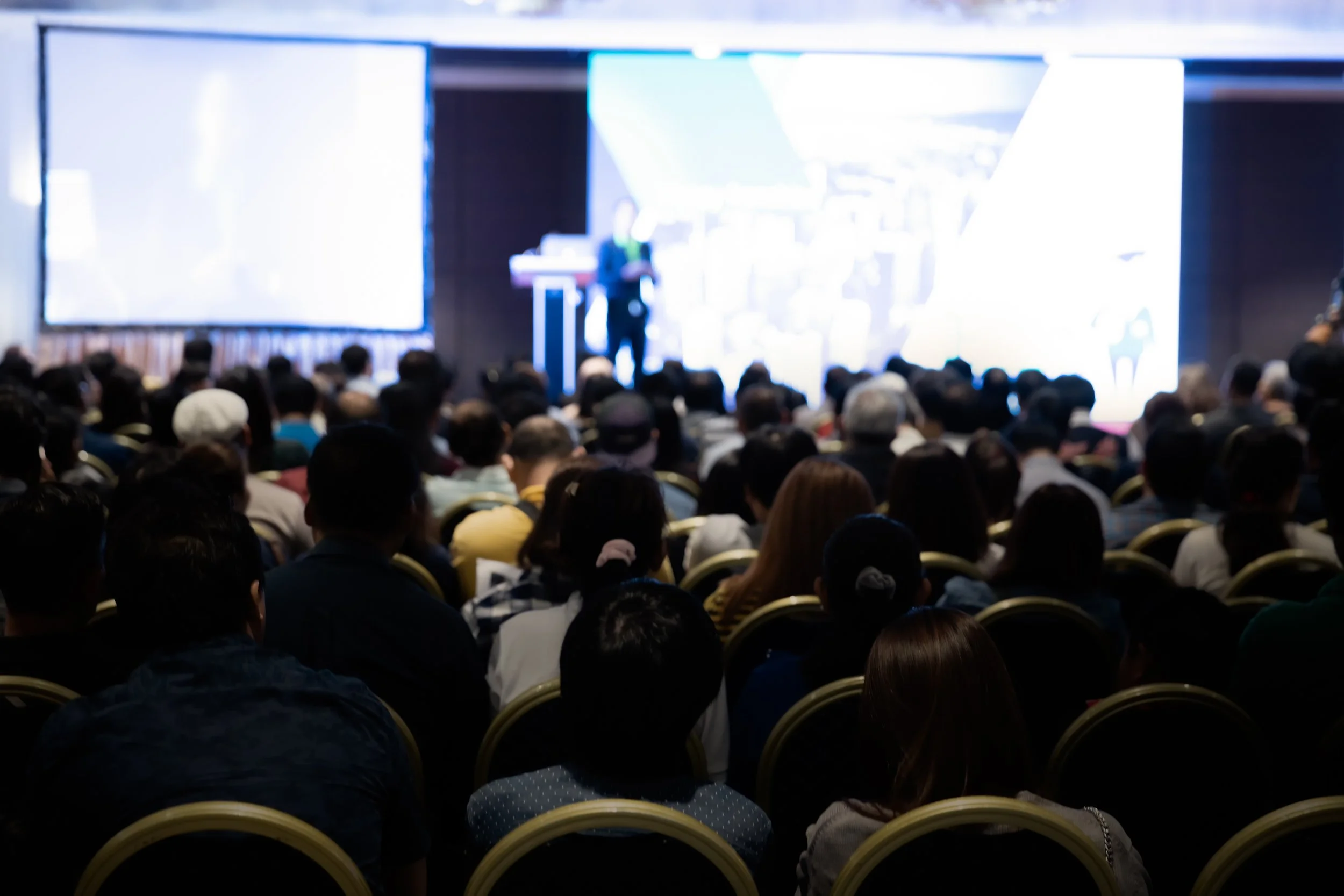 A large audience attending a conference or seminar with a speaker on stage.