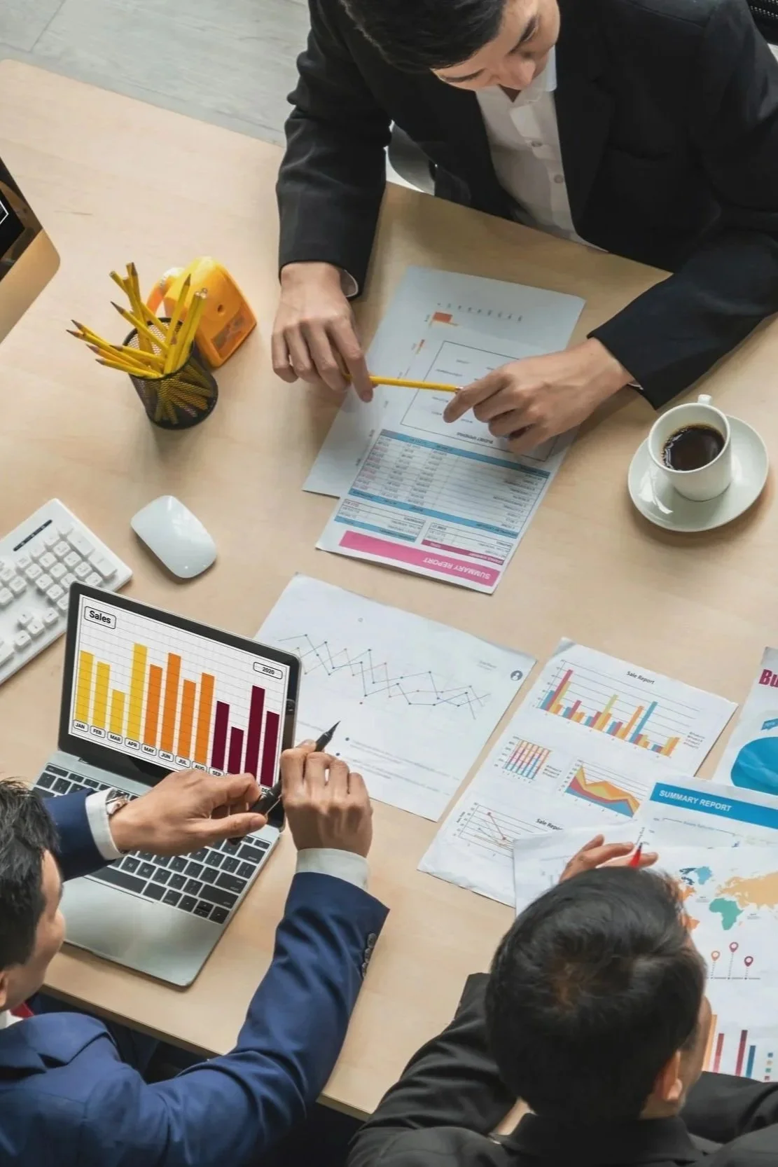 Businesspeople analyzing data and financial reports at a meeting, with charts, graphs, a laptop, and coffee on the table.