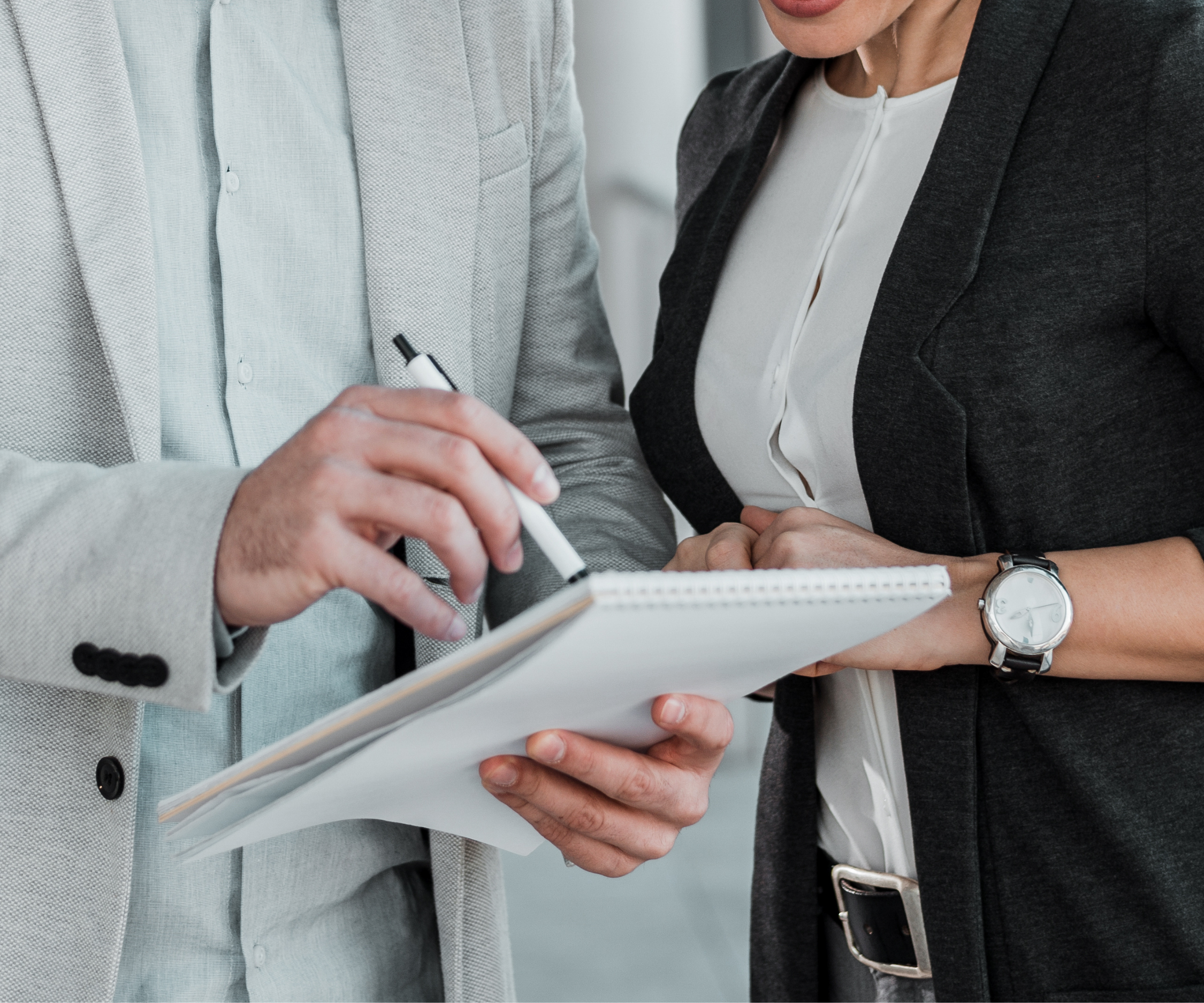 Two people in business attire reviewing documents and writing on a notepad.