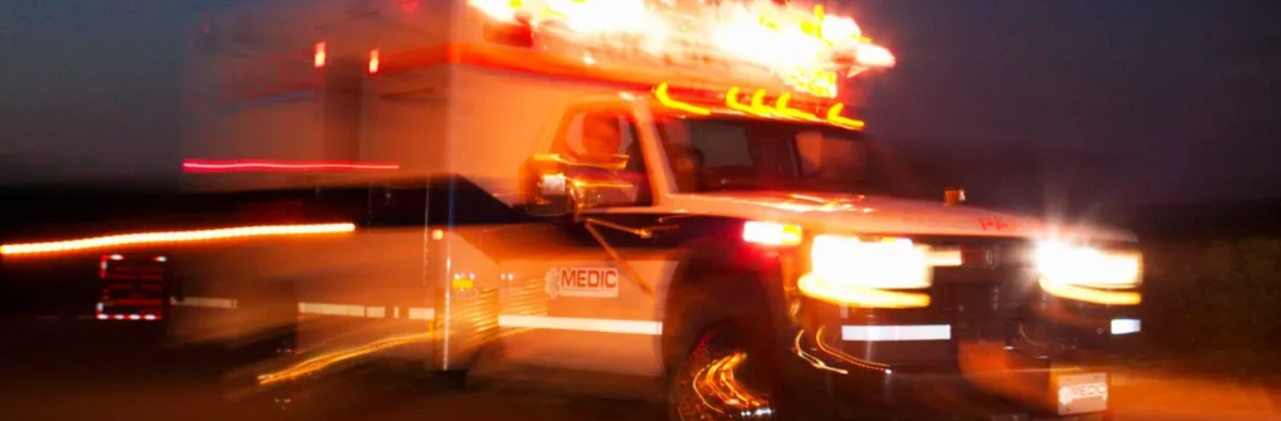 A moving ambulance with flashing lights during night time.