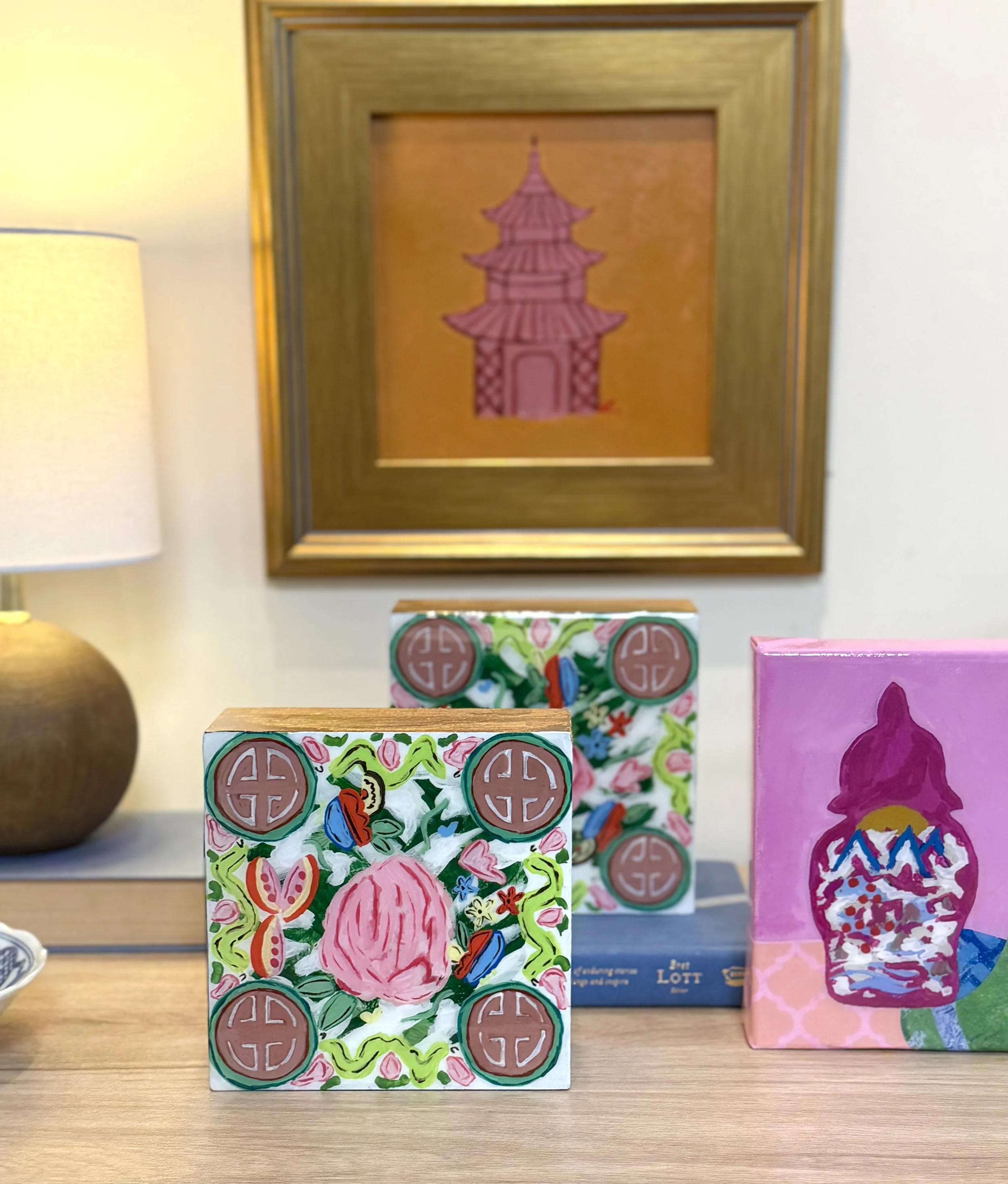 Colorful hand-painted artwork depicting a pink peony surrounded by green leaves and colorful details, set against a background with Buddhist symbols