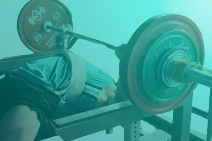 Person performing a bench press with a barbell loaded with weight plates in a gym setting.
