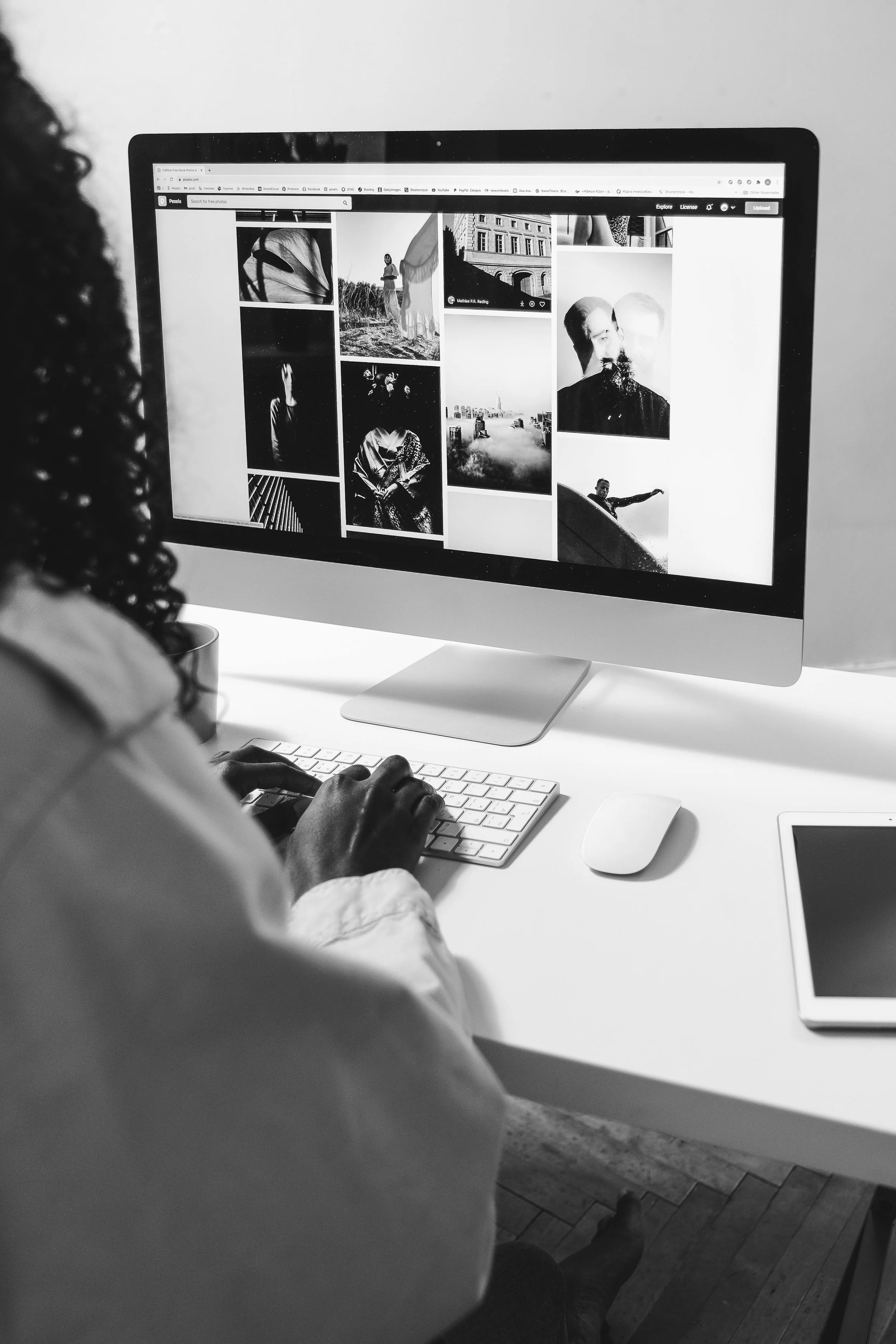 Person browsing black and white photographs on an iMac computer screen, sitting at a white desk.