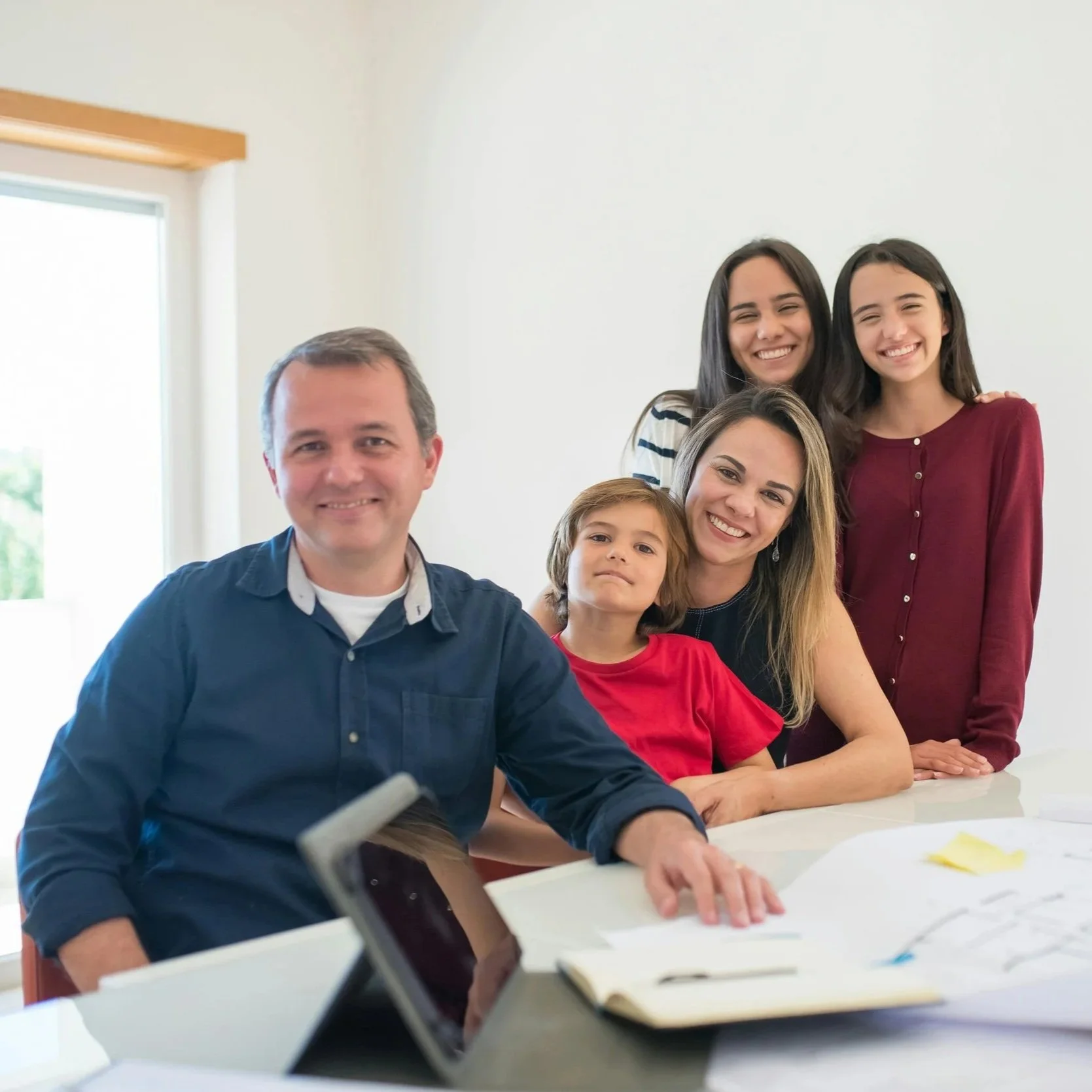A diverse group of five people, including three women, one man, and a young girl, gathered around a white table in a bright room, smiling for a photo.