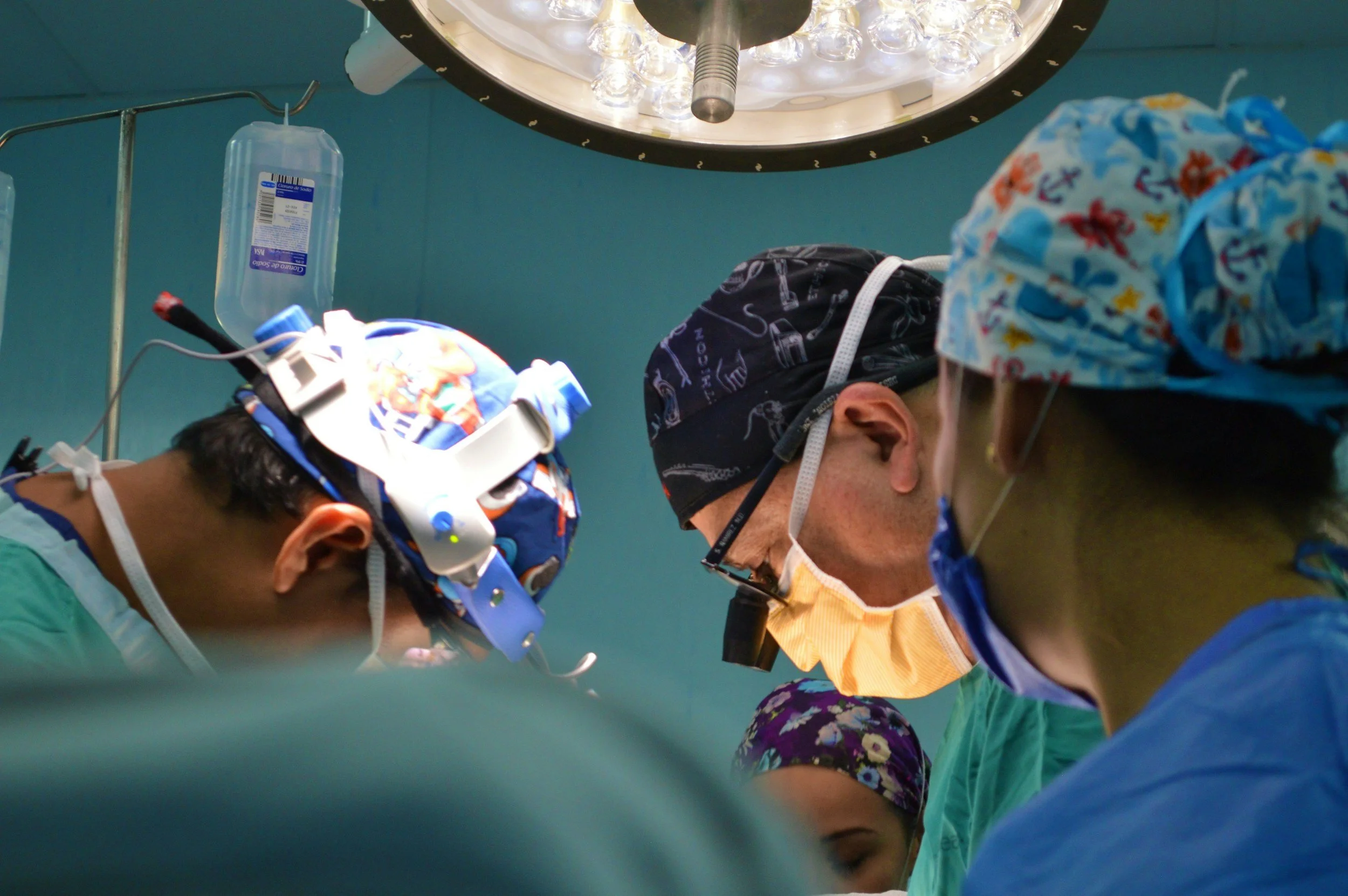Surgeons and medical staff focused during surgery in an operating room, with surgical lights overhead and medical equipment around them.