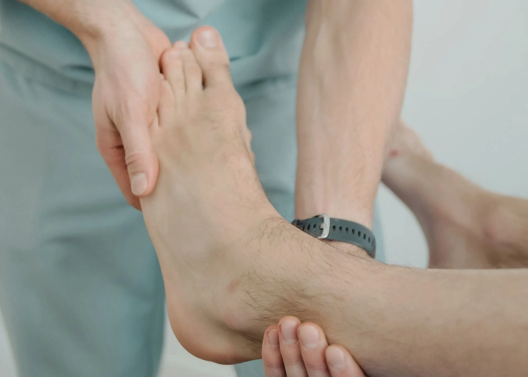 A person holding another person's arm during a medical or physical examination, with their fingernails visible and wearing a wristwatch.