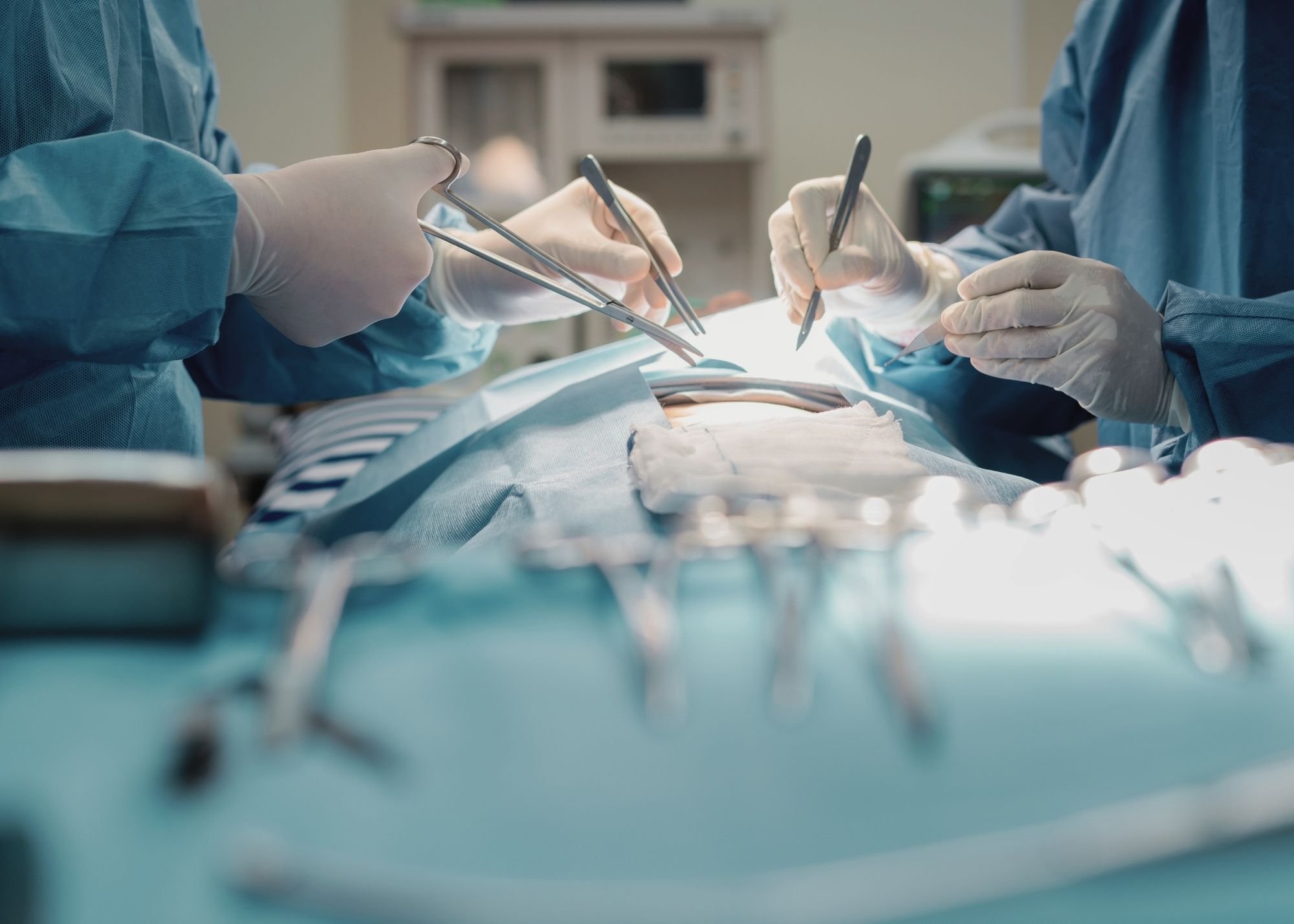 Surgeons in blue scrubs and gloves performing surgery in an operating room.