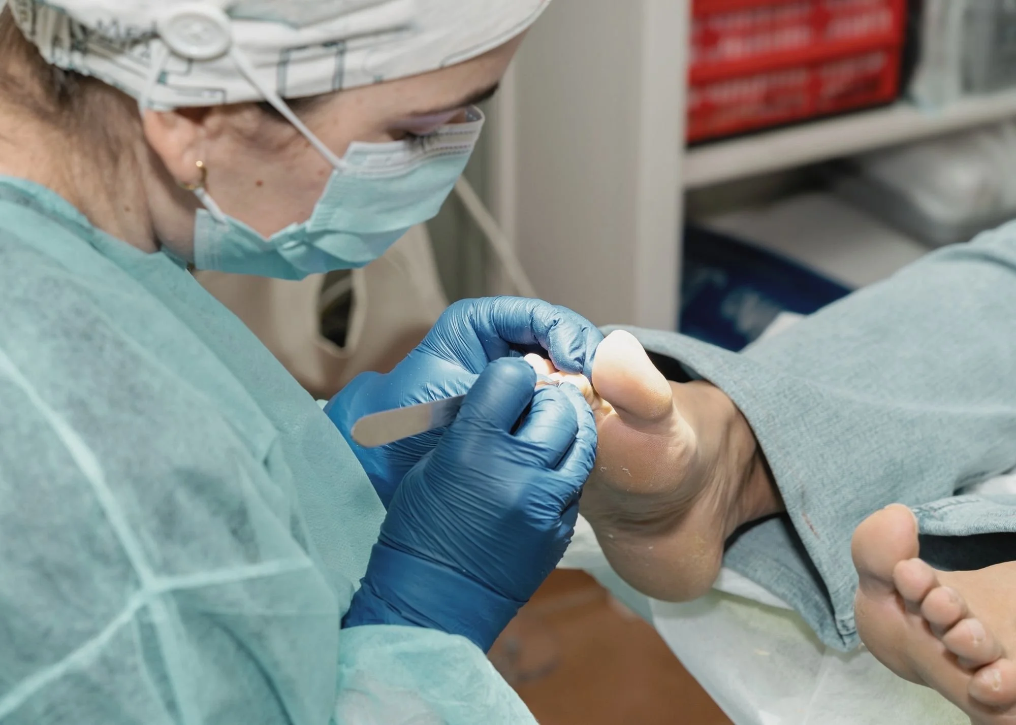 A healthcare professional in scrubs, a surgical cap, face mask, and gloves, performing a dental procedure on a patient in a medical setting.