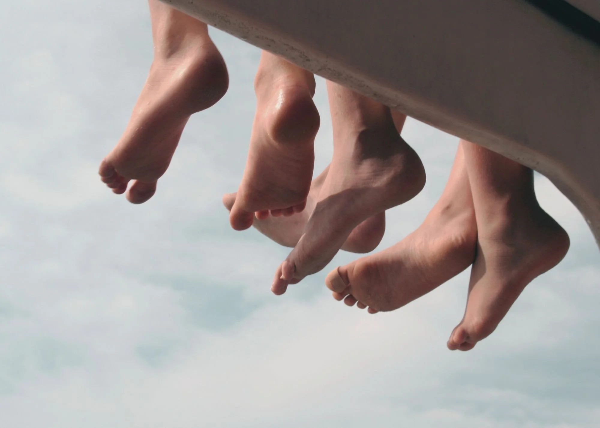 Close-up of multiple human hands reaching downward against a cloudy sky.