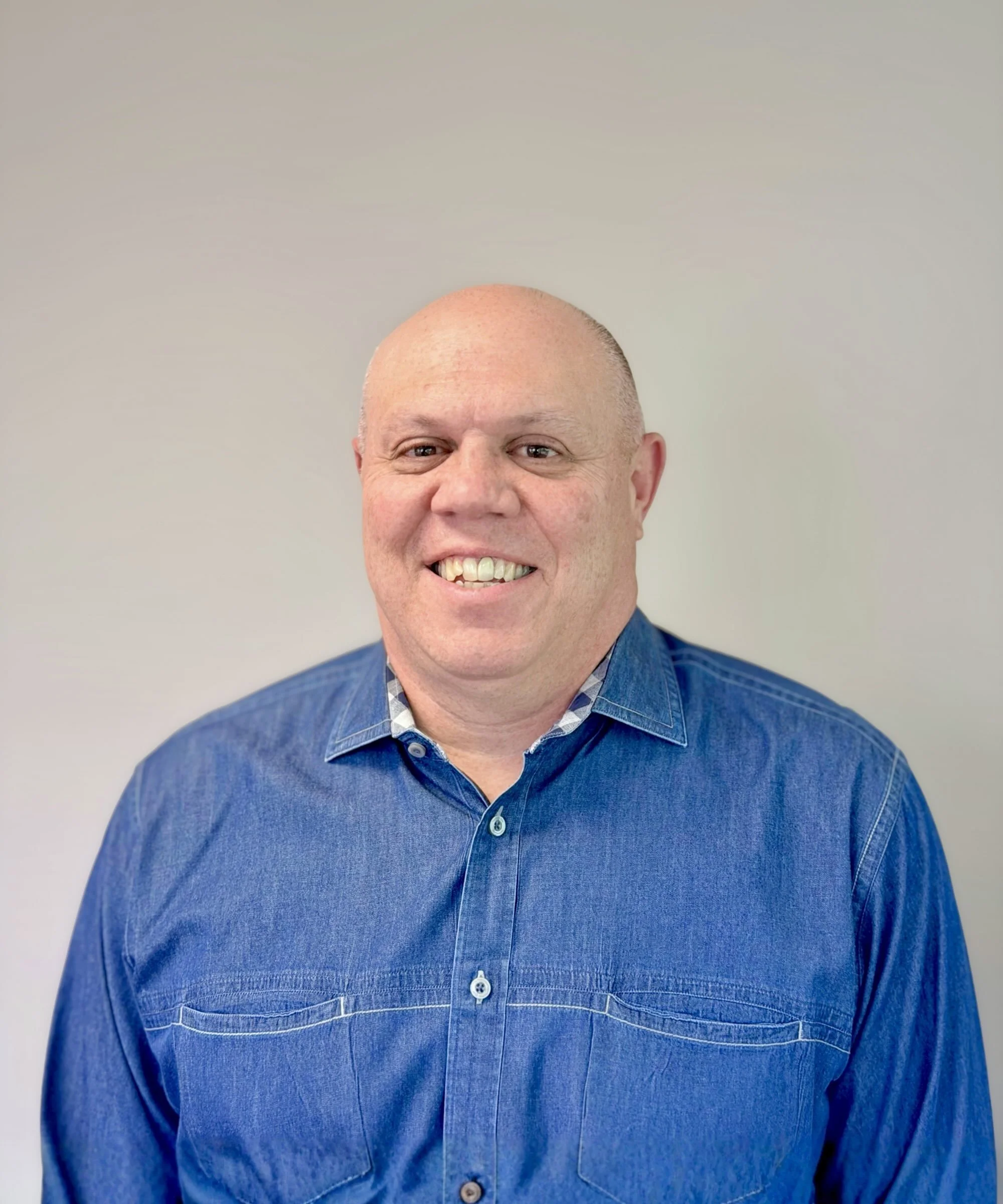 Close-up of a smiling man with a shaved head wearing a blue shirt.