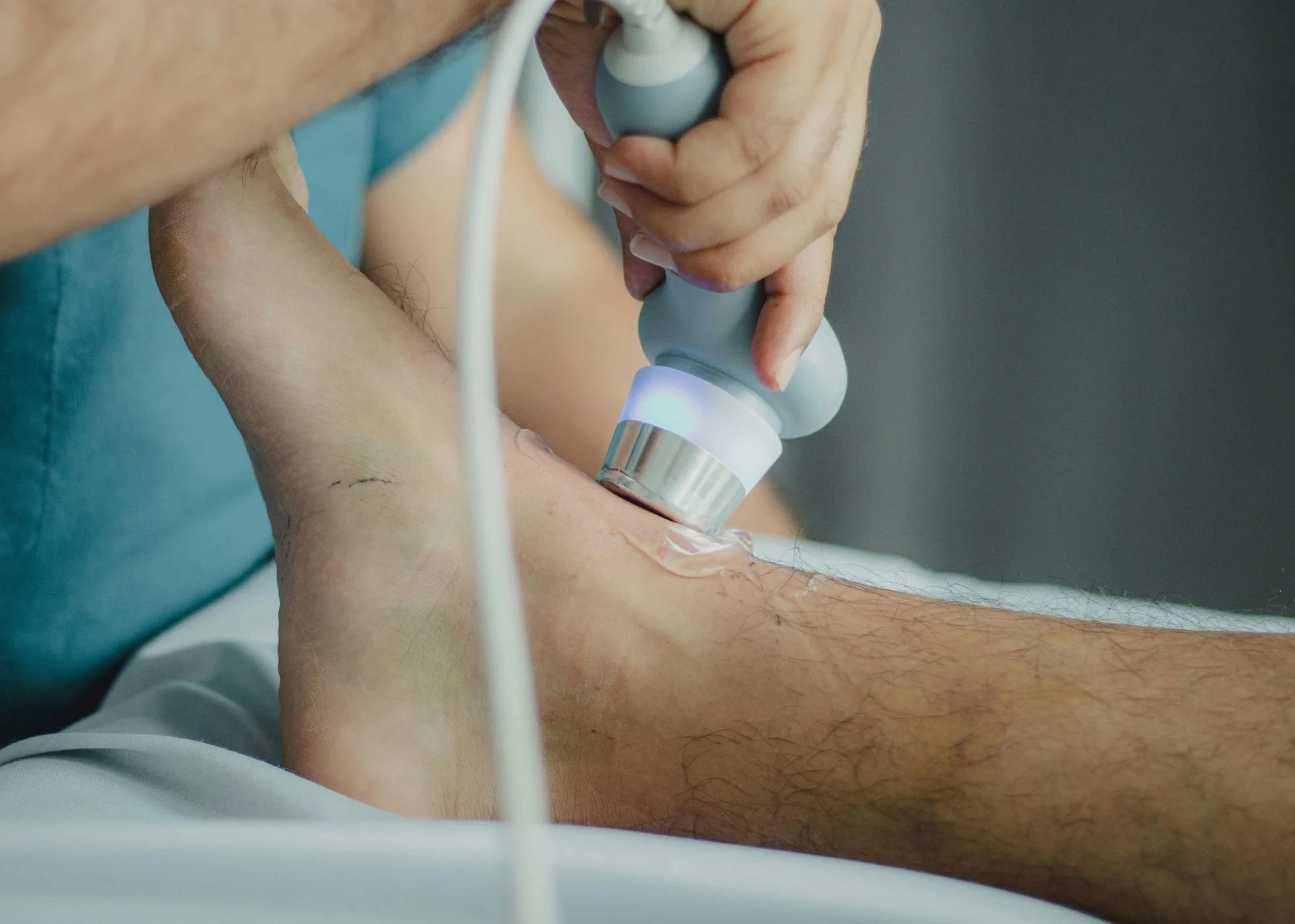 A person undergoing a medical ultrasound exam, with the ultrasound probe pressed against their leg while a healthcare professional operates the device.