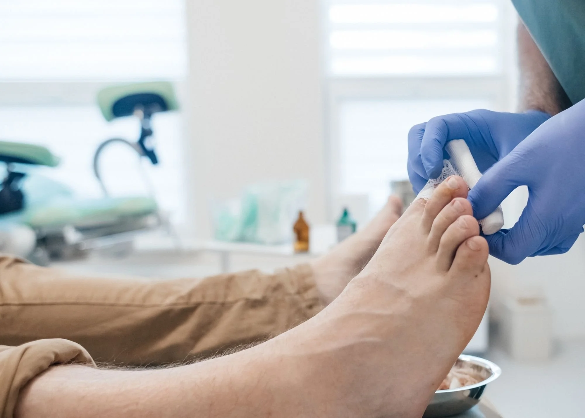 A person receiving medical care, with a healthcare professional wearing blue gloves and applying a bandage to the person's finger in a clinical setting.