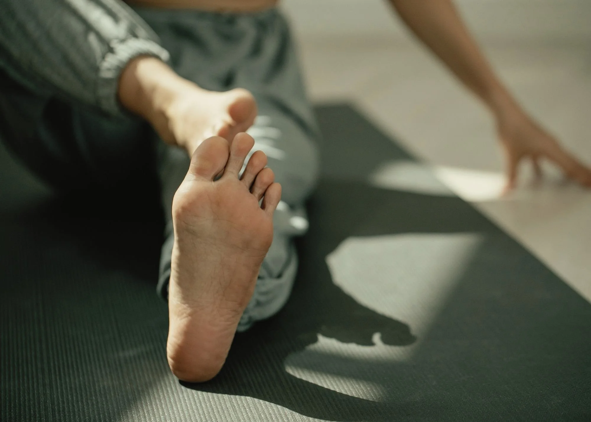 Close-up of a person's foot resting on a black yoga mat, with a skeleton ankle and foot model in the background during exercise or physical therapy.